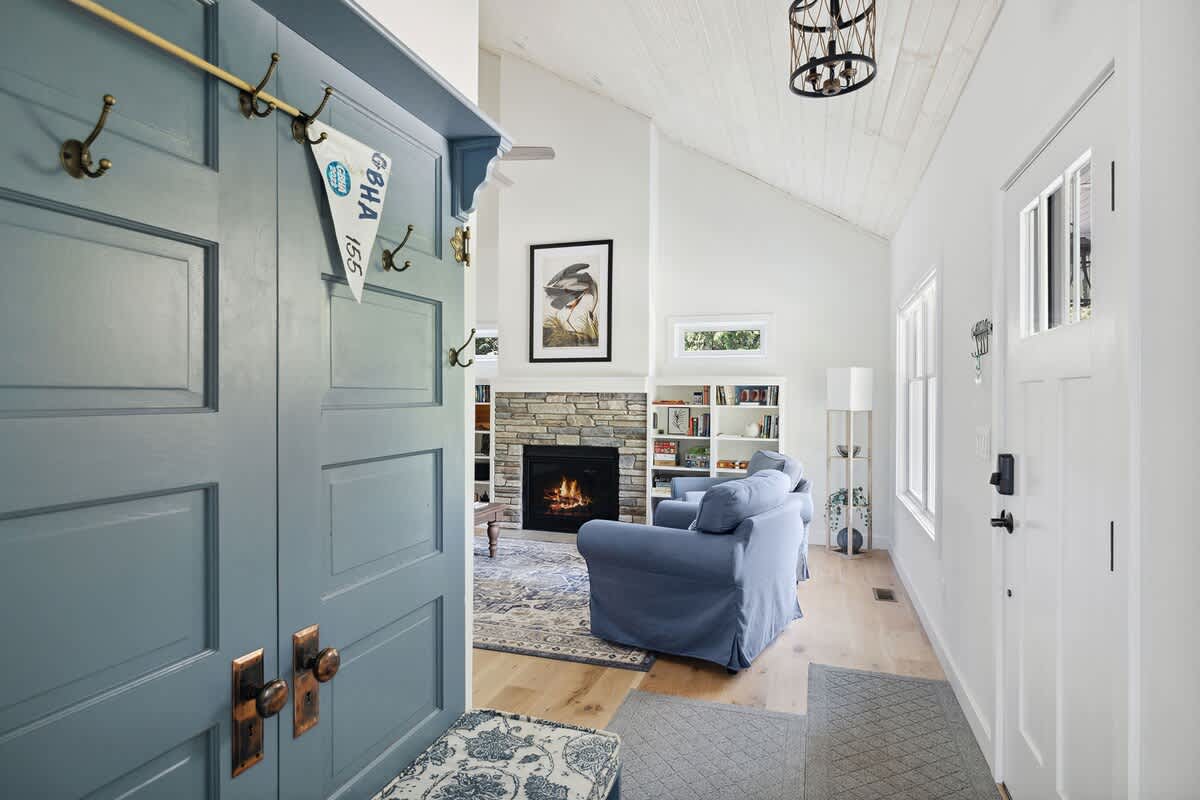 Entryway with a large blue built-in coat rack and bench, offering a glimpse into a bright living room with a stone fireplace and high vaulted ceilings.
