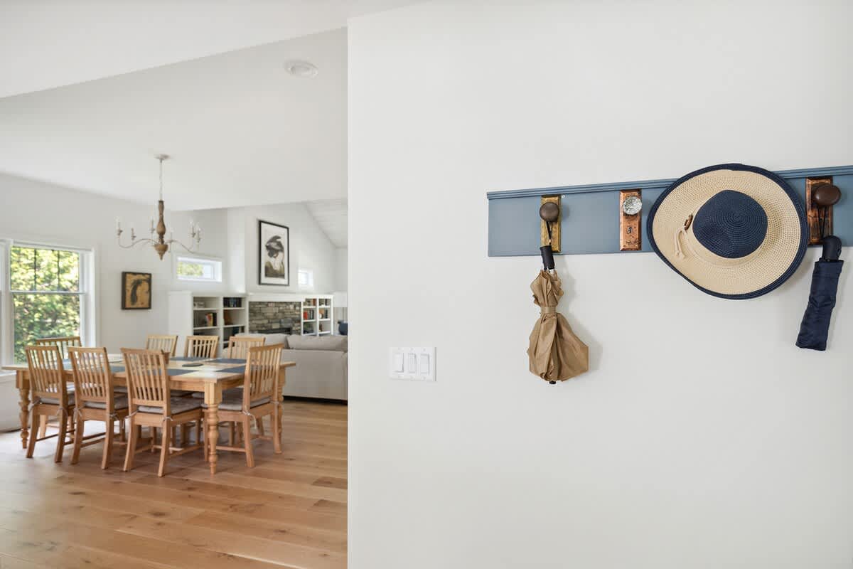 Spacious dining area featuring a large wooden dining table with seating for eight, illuminated by a chandelier, and openly connected to a living room with a stone fireplace.
