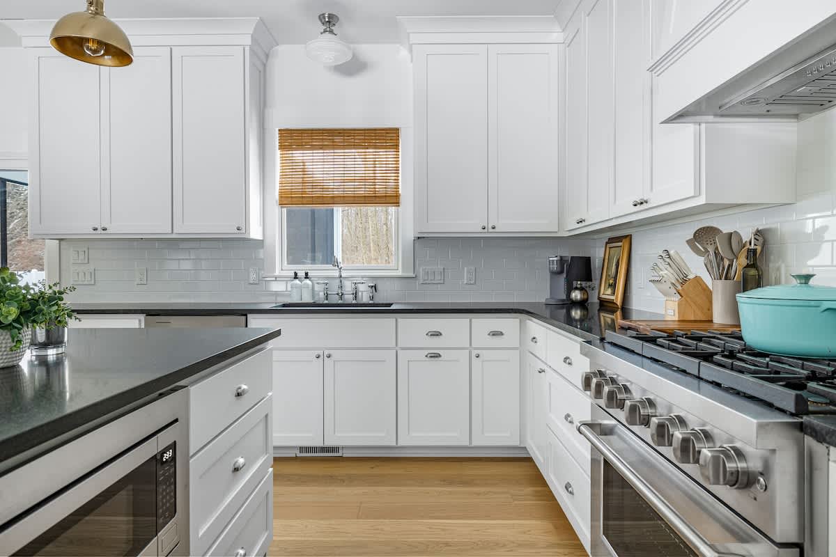 A spacious kitchen features white shaker cabinets, dark countertops, and a white subway tile backsplash. A stainless steel range with a matching hood is visible, along with a microwave built into the kitchen island.