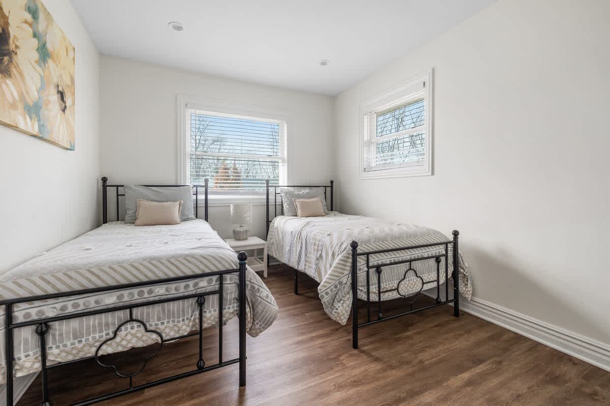 Another view of the bedroom with two twin beds, black metal frames, and striped bedding. Hardwood floors and white walls create a clean, simple aesthetic.