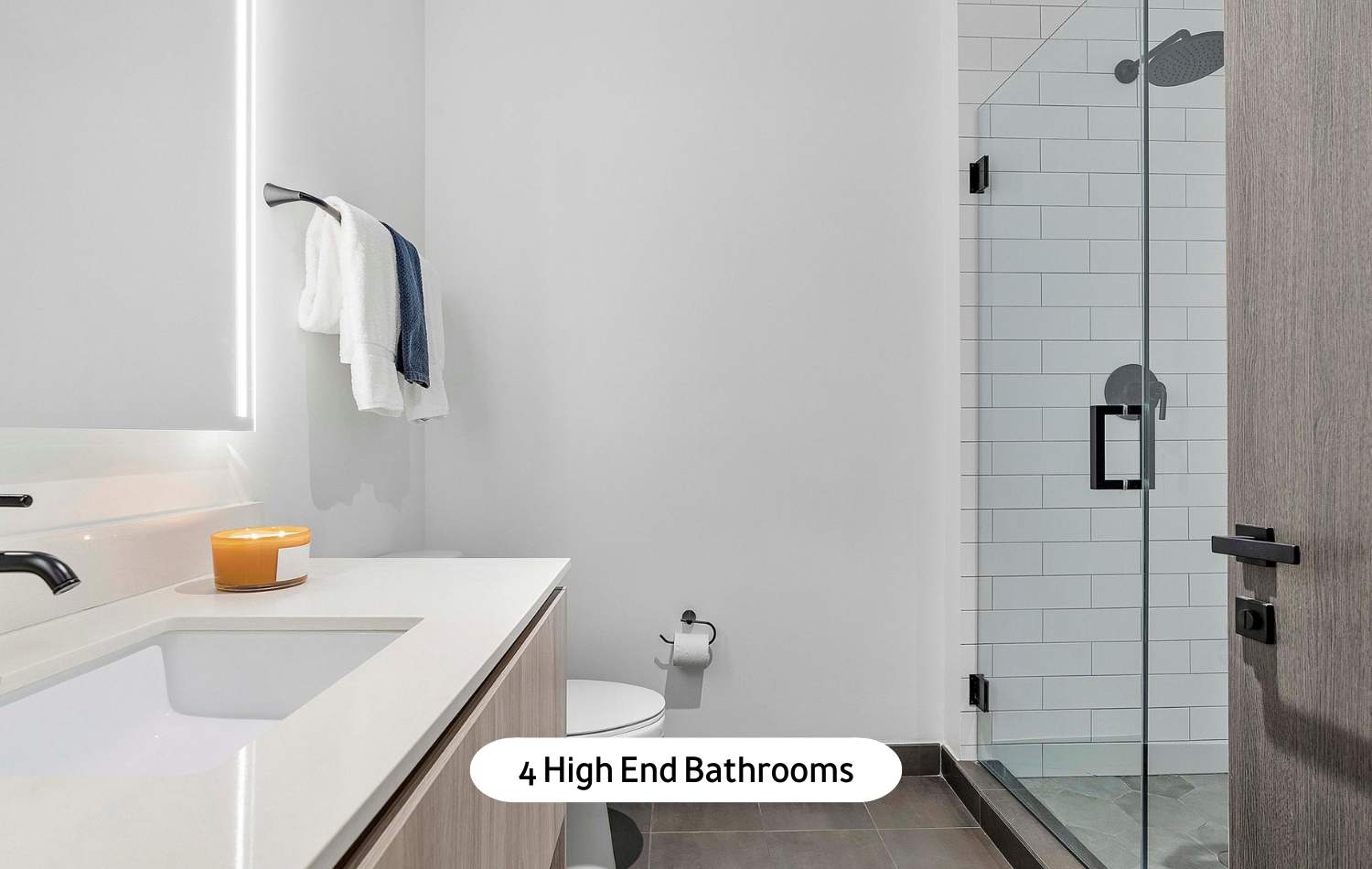 Contemporary bathroom featuring a white vanity with a rectangular sink, a large illuminated mirror, and a spacious glass-enclosed shower with white subway tile walls and dark floor tiles.