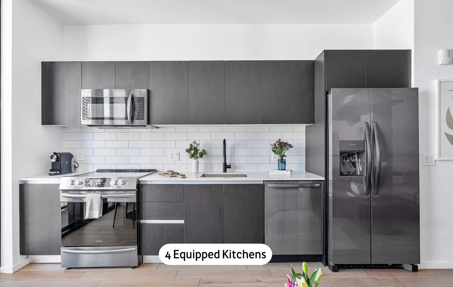 Sleek, modern kitchen featuring dark grey flat-panel cabinetry, a white subway tile backsplash, and a full suite of stainless steel appliances including a refrigerator, microwave, oven, and dishwasher.