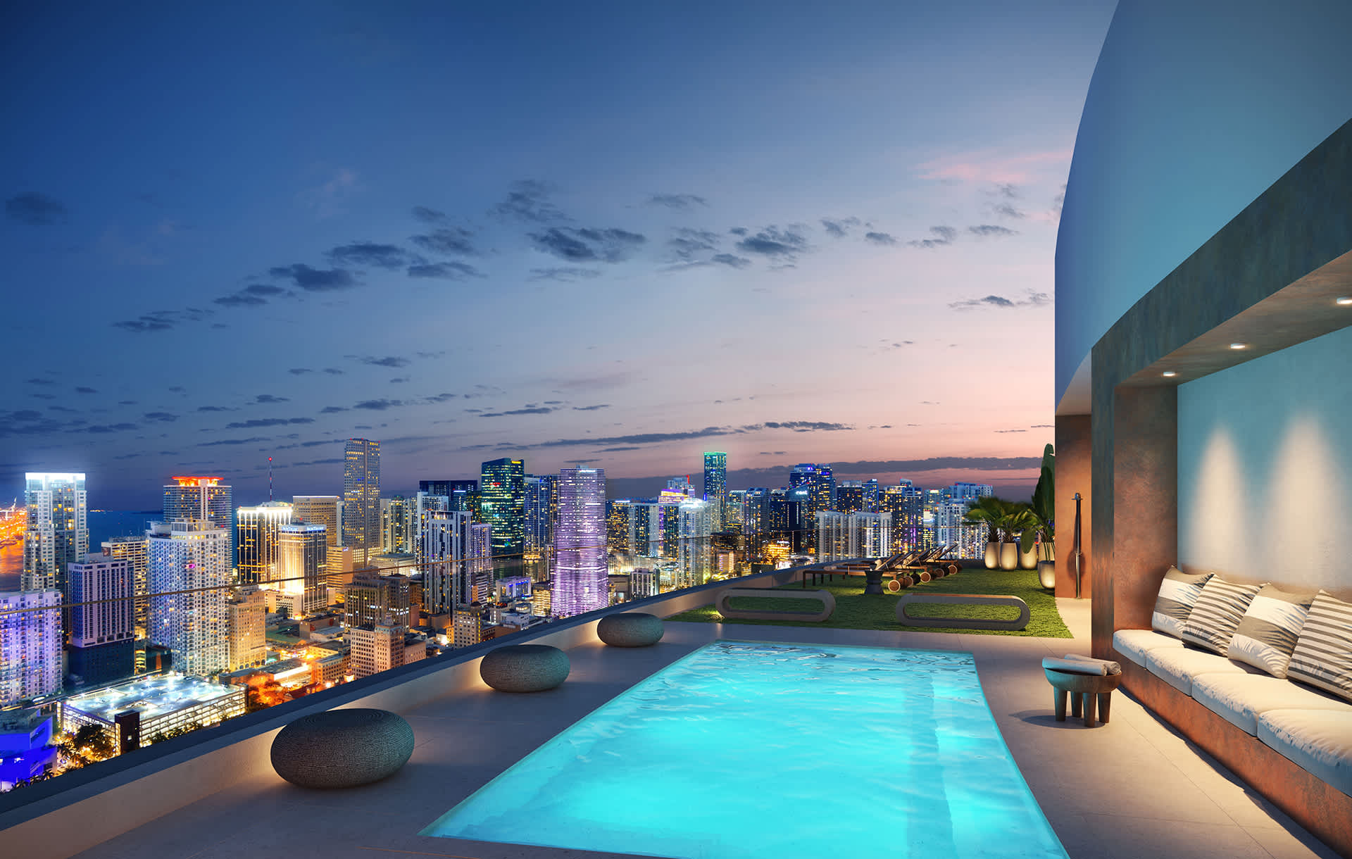 A vibrant rooftop pool area glows at night, featuring a rectangular pool, lounge seating with cushions, and breathtaking illuminated city skyline views against a twilight sky.