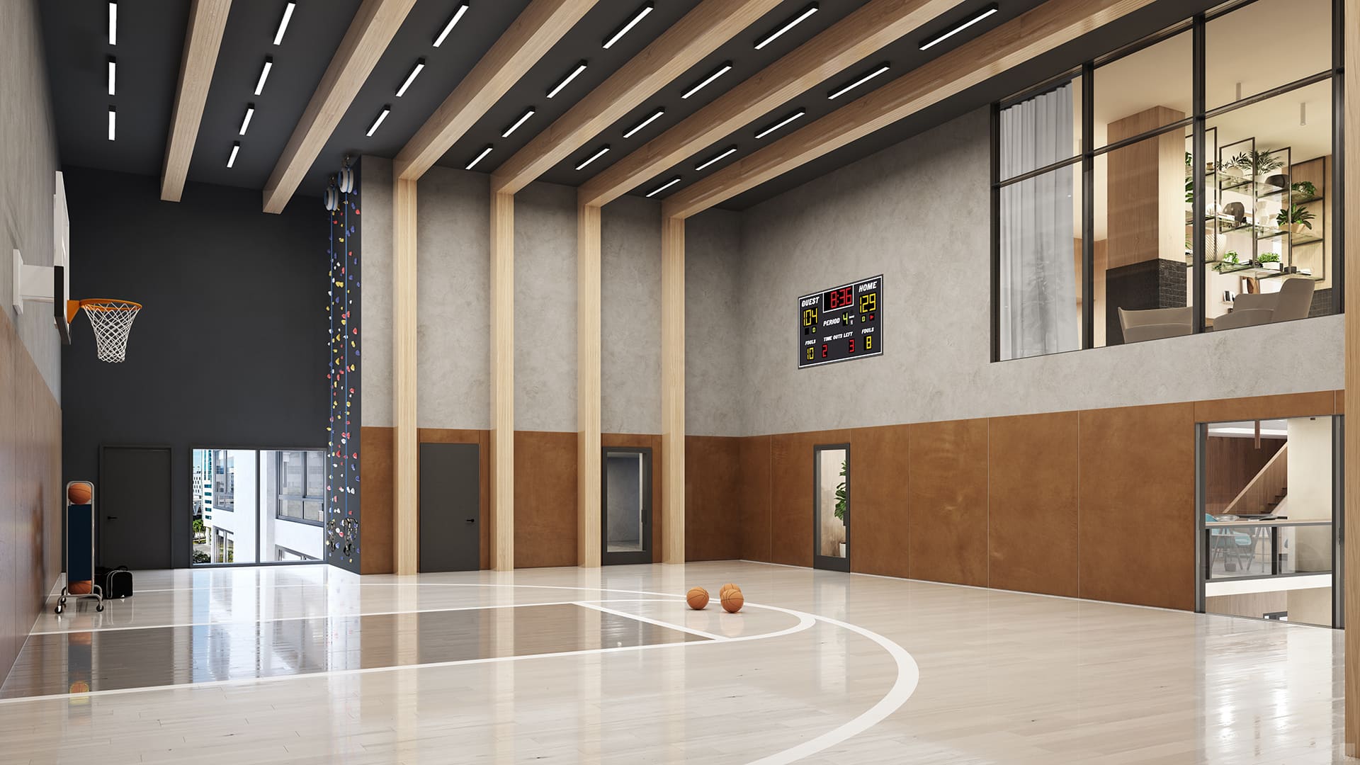 A bright indoor basketball court with polished wooden floors and a hoop, also features a climbing wall and a scoreboard, set within a modern space with high ceilings and large windows.