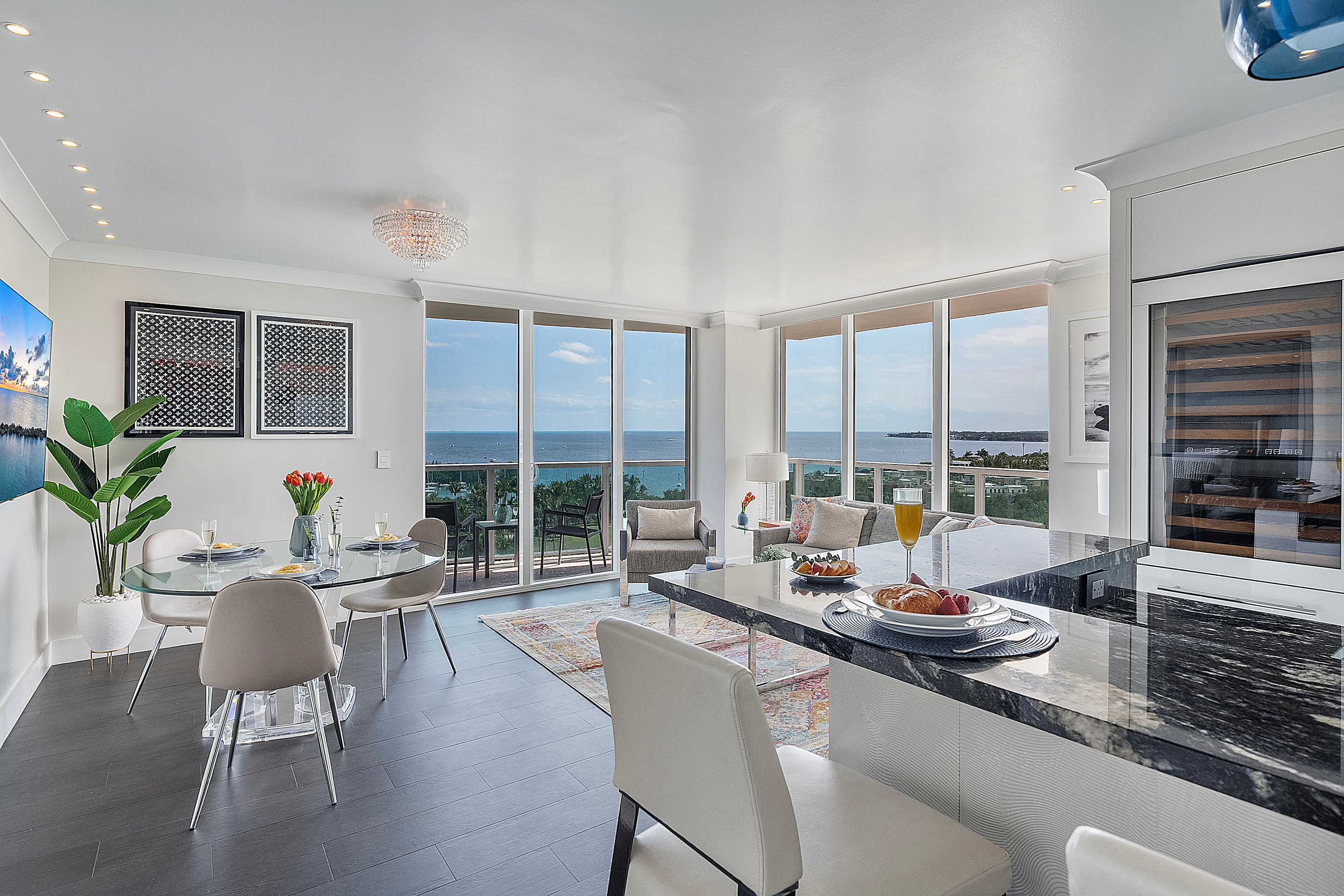An open-plan living space showcasing a modern kitchen island with bar seating, a glass dining table, and a comfortable living area, all bathed in natural light from large windows with stunning ocean views.