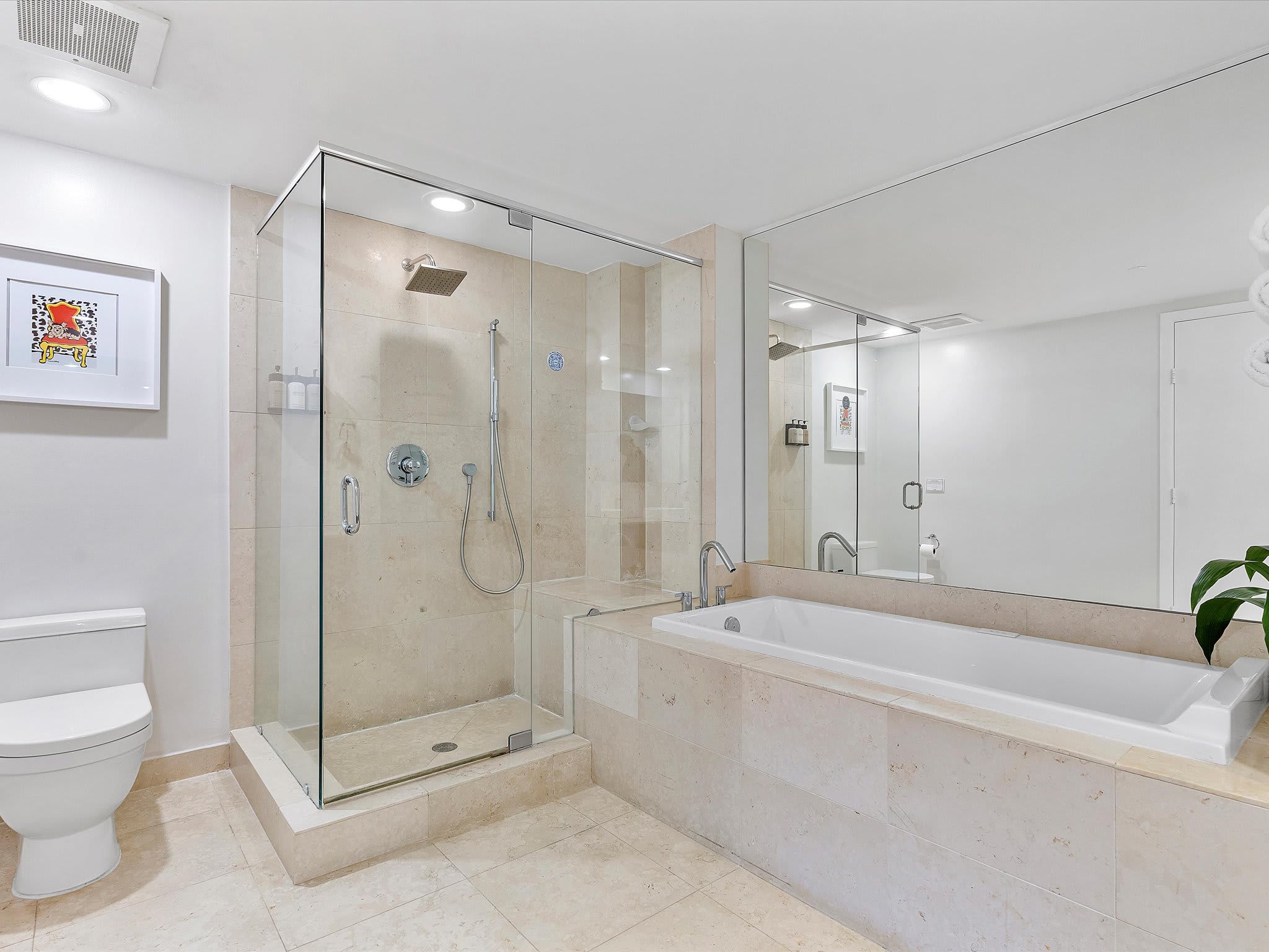 Modern bathroom featuring light-colored tiled walls and floor, a glass-enclosed walk-in shower with a rain showerhead, and a built-in bathtub with a chrome faucet. A large mirror spans the wall above the tub, reflecting the room.