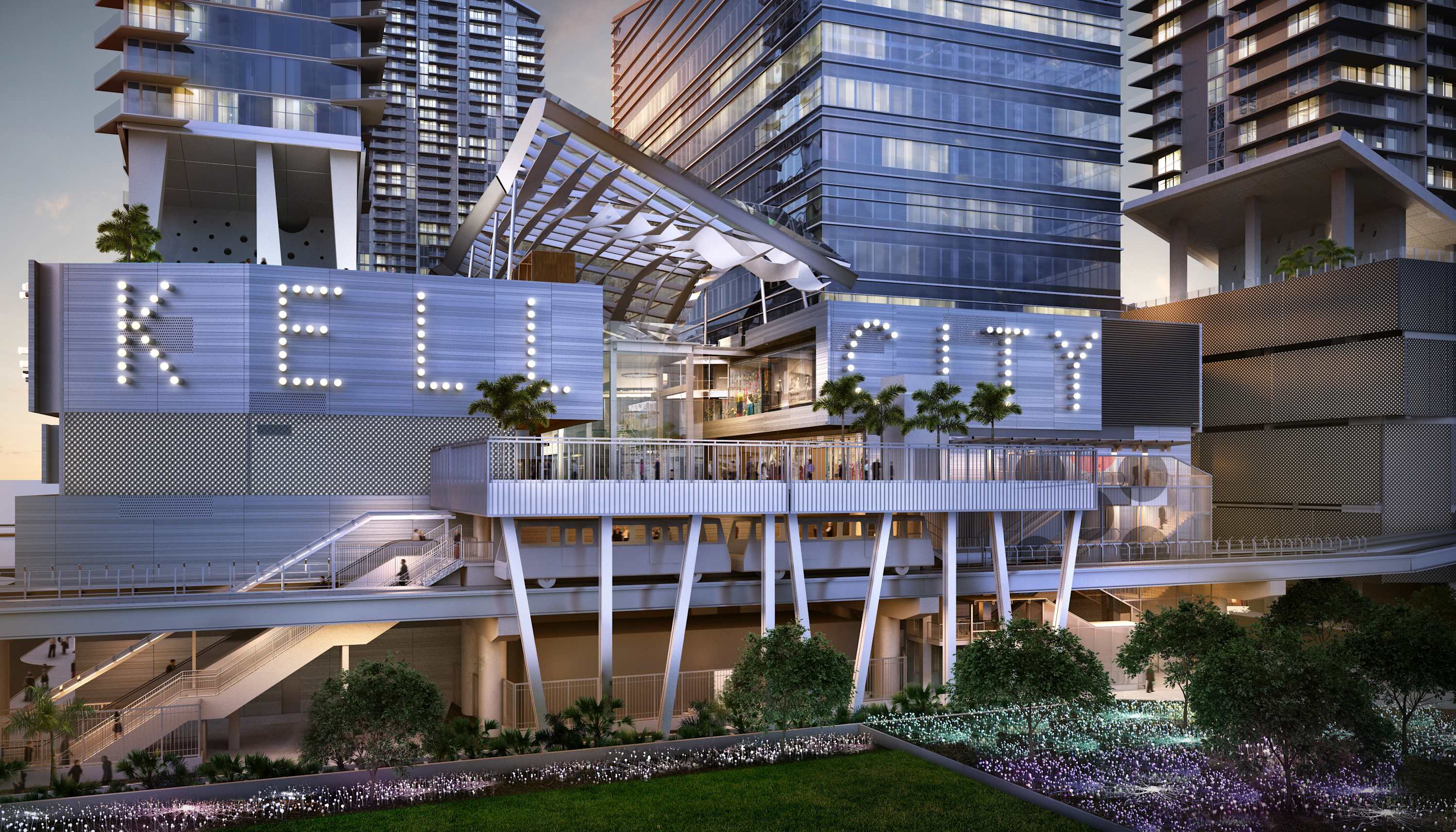 Modern urban building complex with prominent "BRICKELL CITY" signage illuminated by lights, featuring contemporary architecture and a raised train track. Lush landscaping with palm trees and decorative lighting enhances the exterior.