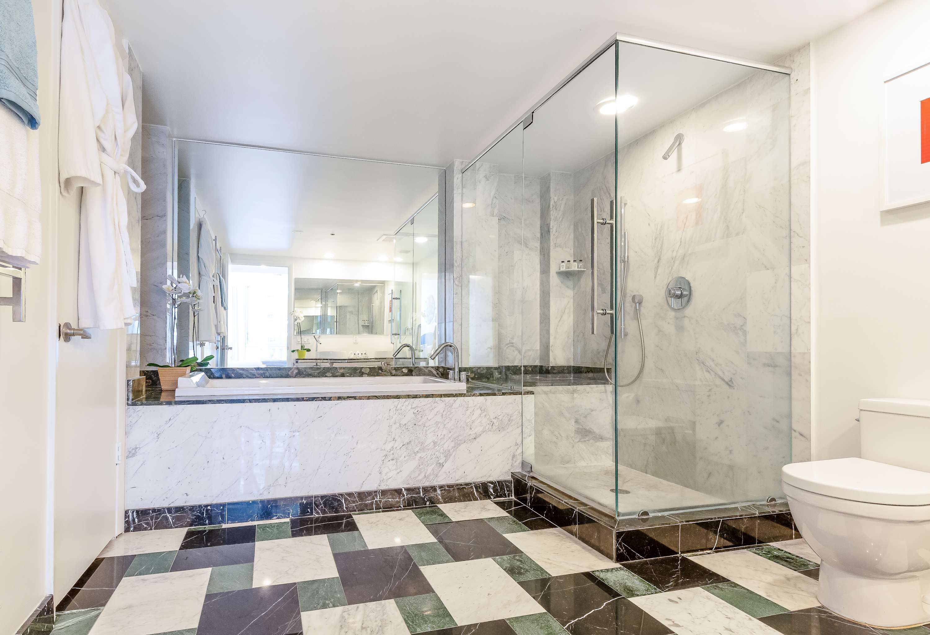 Luxurious bathroom with a large soaking tub integrated into a marble surround, a separate glass-enclosed walk-in shower, and a toilet. The floor features a black, white, and green checkered marble pattern, matching bathroom-1.