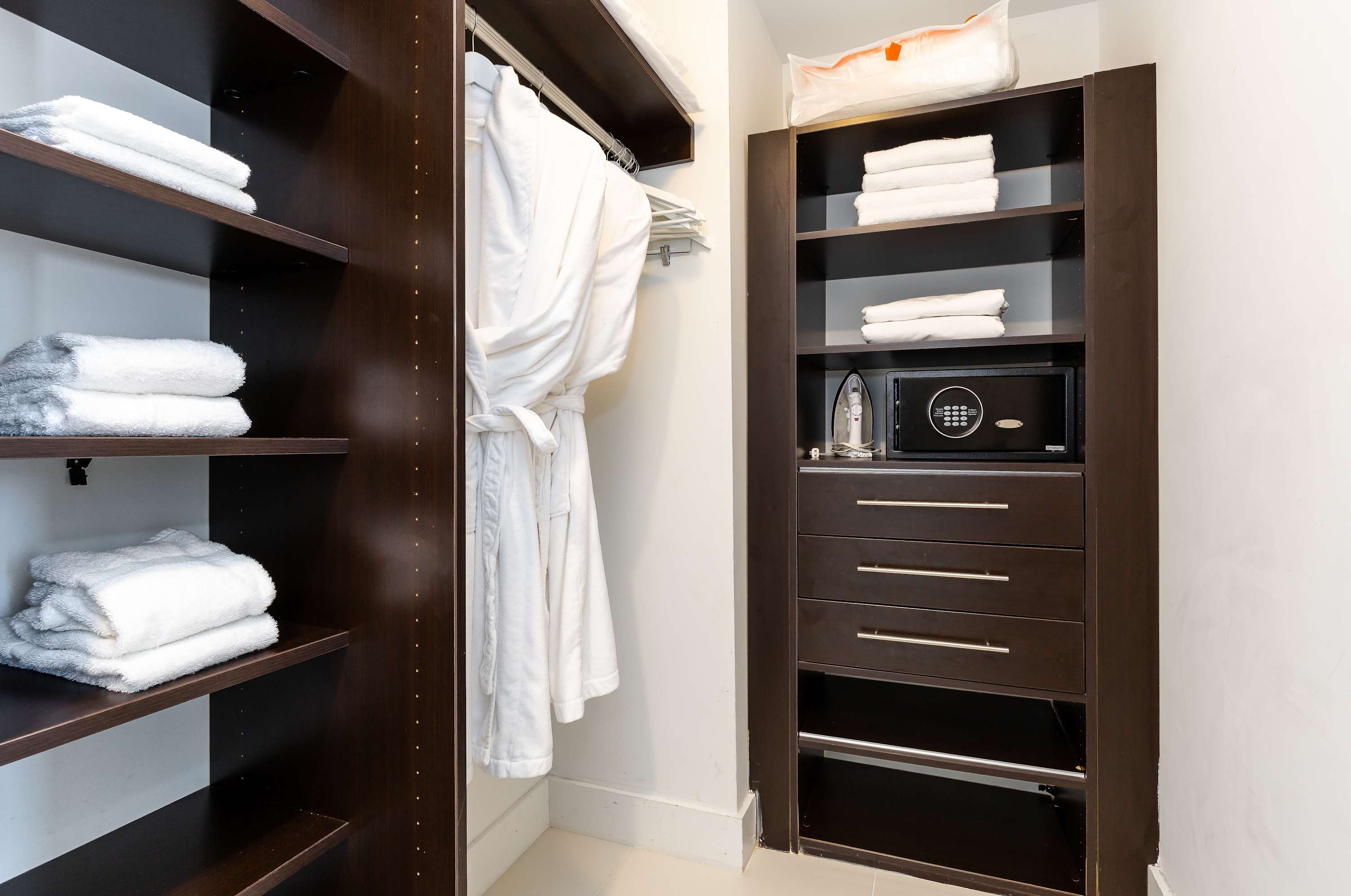 A well-organized walk-in closet with dark wood shelving units, providing ample storage for clothes and towels, and featuring a small safe.