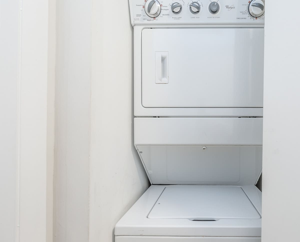 A compact laundry area features a stacked white Whirlpool washer and dryer unit, neatly tucked into a closet space. The appliances appear clean and well-maintained, ready for guest use.