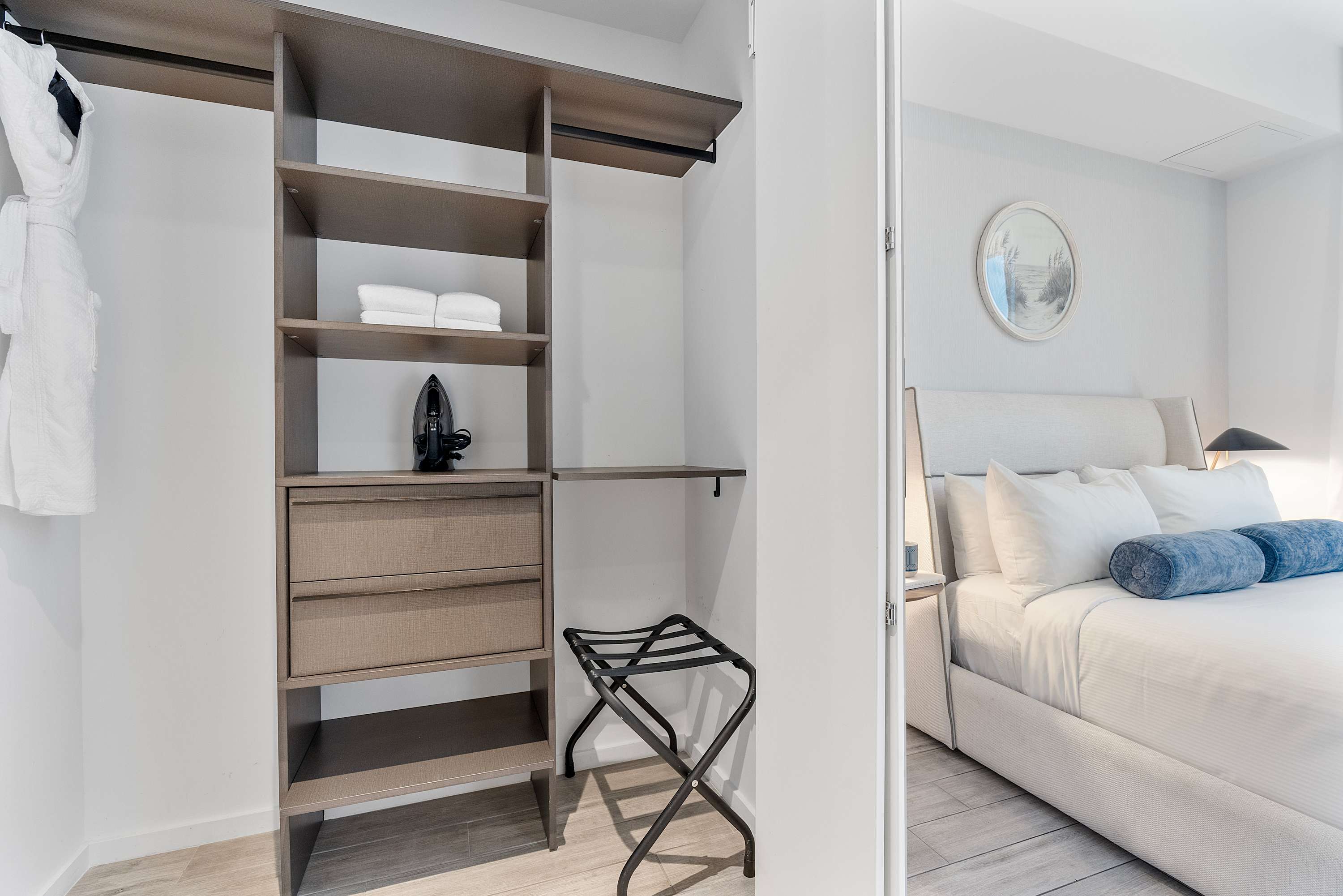 Open closet area with built-in shelving, drawers, and hanging space, featuring a luggage rack and an iron. It is located within or adjacent to Bedroom-2, visible through the doorway.