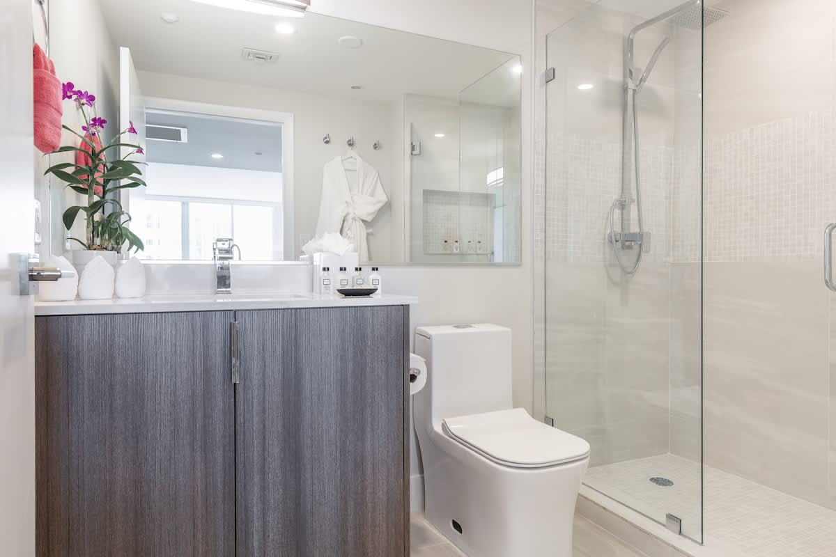 Contemporary bathroom featuring a floating wood-grain vanity with a white countertop and sink, a modern toilet, and a glass-enclosed walk-in shower with light tiled walls.