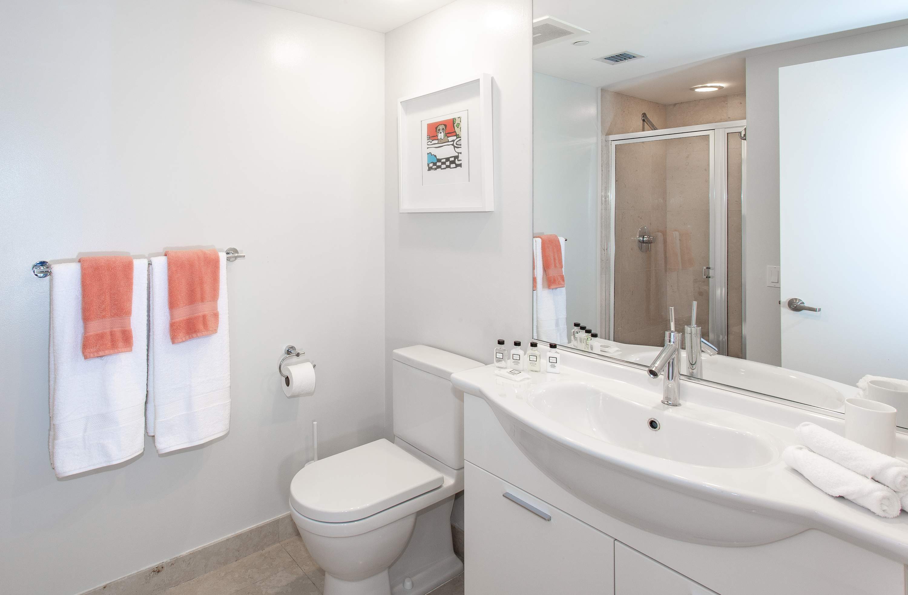 Bright modern bathroom featuring a white toilet, a contemporary white vanity with an integrated sink, and a large mirror. Orange and white towels are neatly folded on a rack next to the toilet.