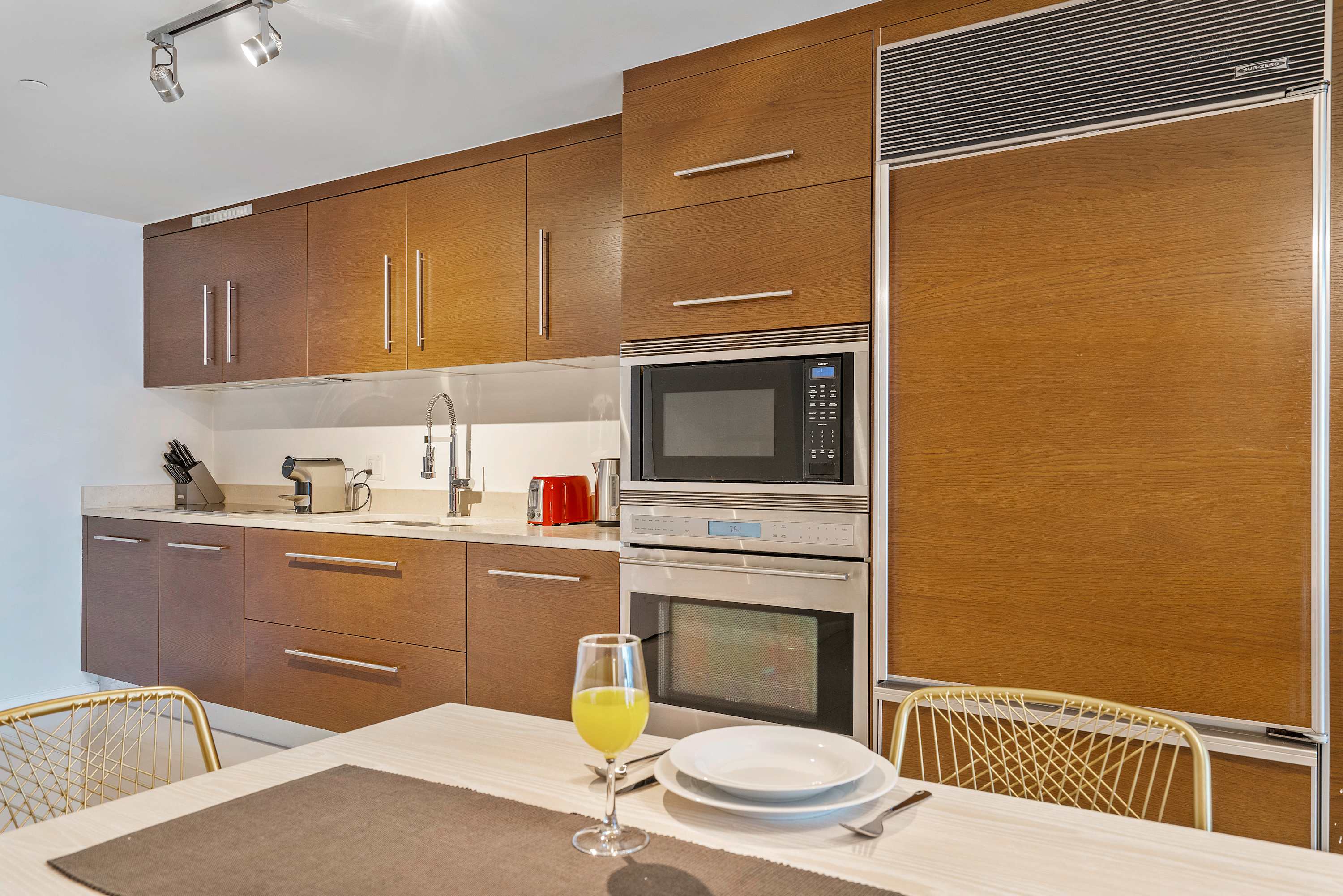 Modern kitchen with rich wood cabinetry, white countertops, and integrated stainless steel appliances including a microwave, oven, and refrigerator, with a sink and small appliances visible.