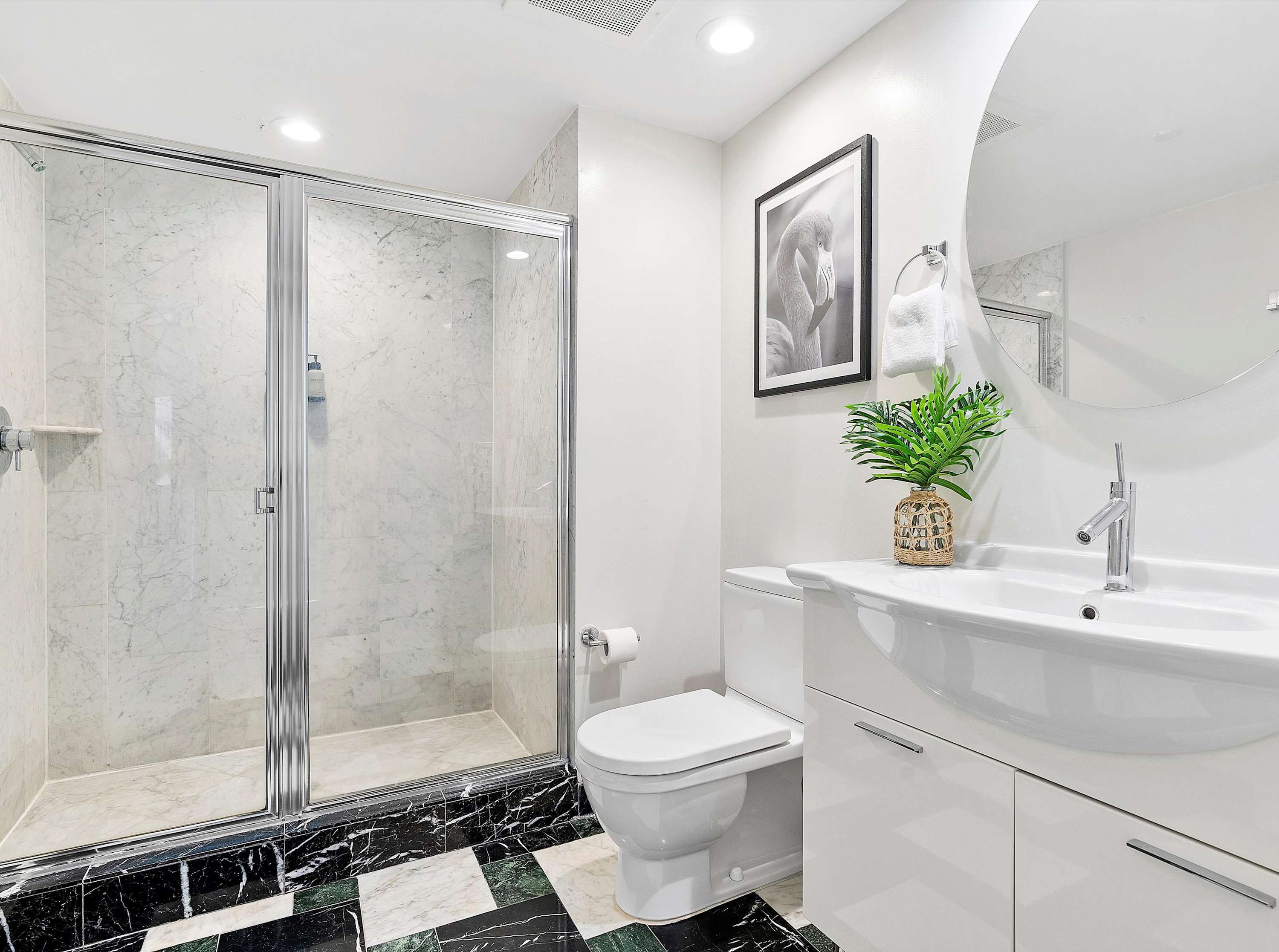 Modern bathroom with a glass-enclosed shower featuring white marble tiles, a white toilet, and a white vanity with a sink, all set against a striking black and green checkered floor.