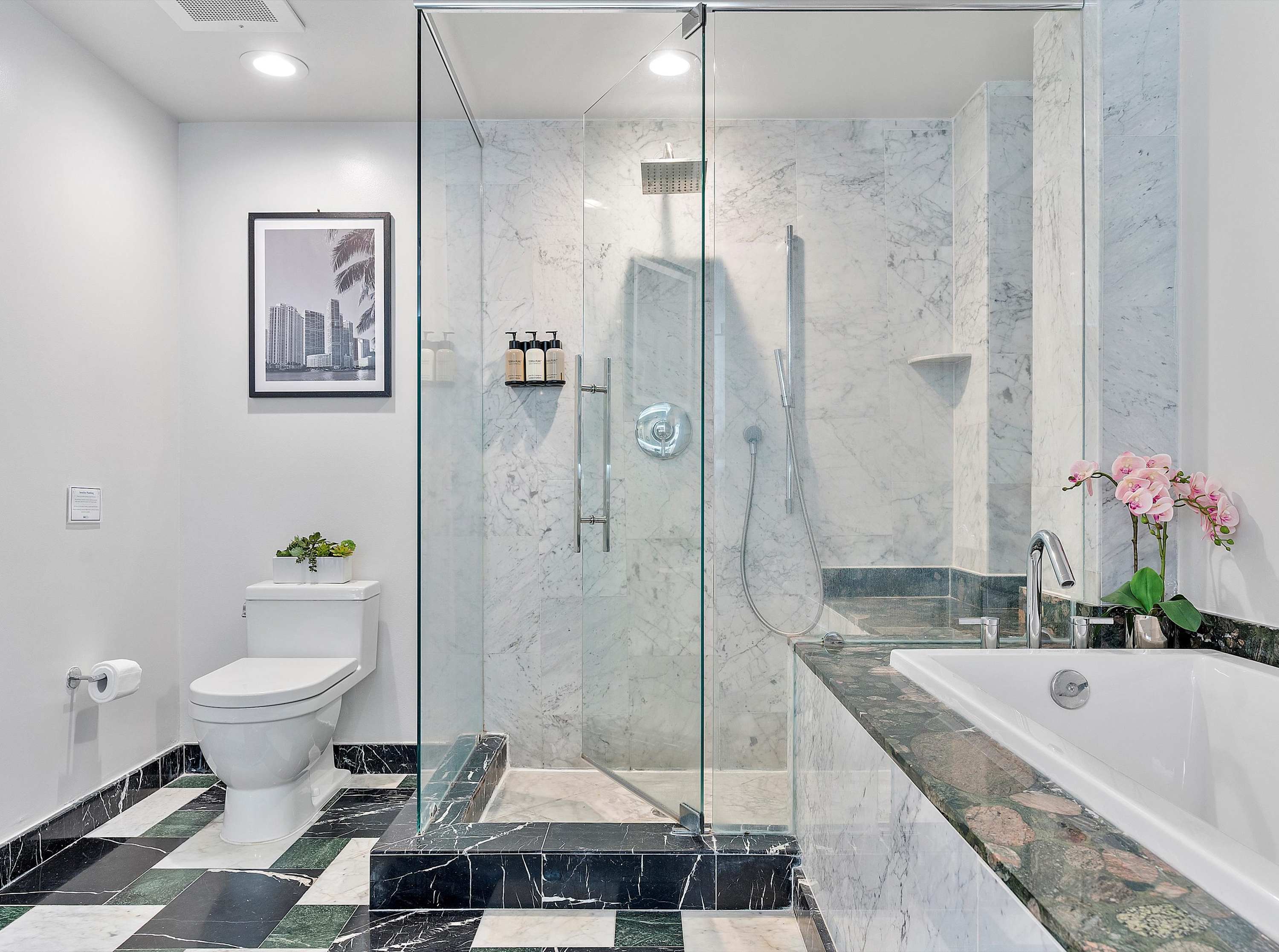 Bright bathroom showcasing a white toilet, a glass-enclosed walk-in shower with marble tiling, and a built-in soaking tub, all set on a striking checkered marble floor.