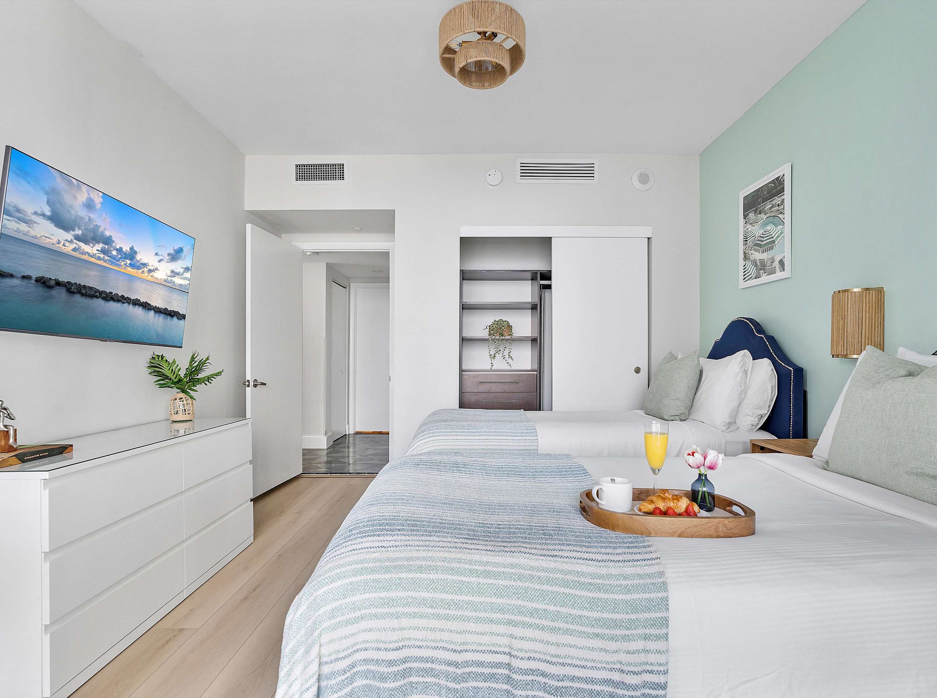 View of the second bedroom showing two twin beds, a wall-mounted TV above a white dresser, and a built-in closet with sliding doors.