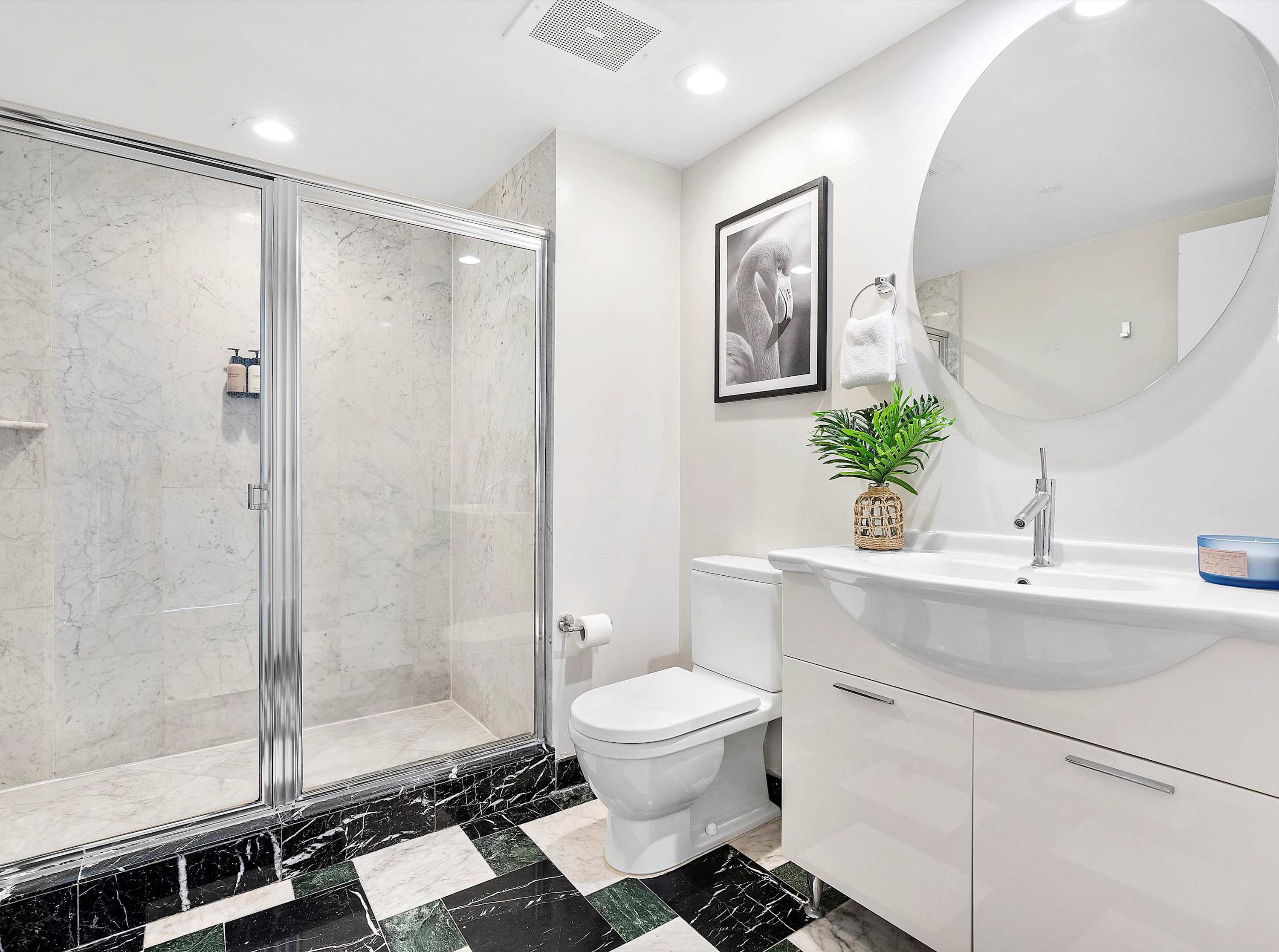 Compact second bathroom featuring a white single vanity with a round mirror, a glass-enclosed walk-in shower, and a black and green checkered marble floor.