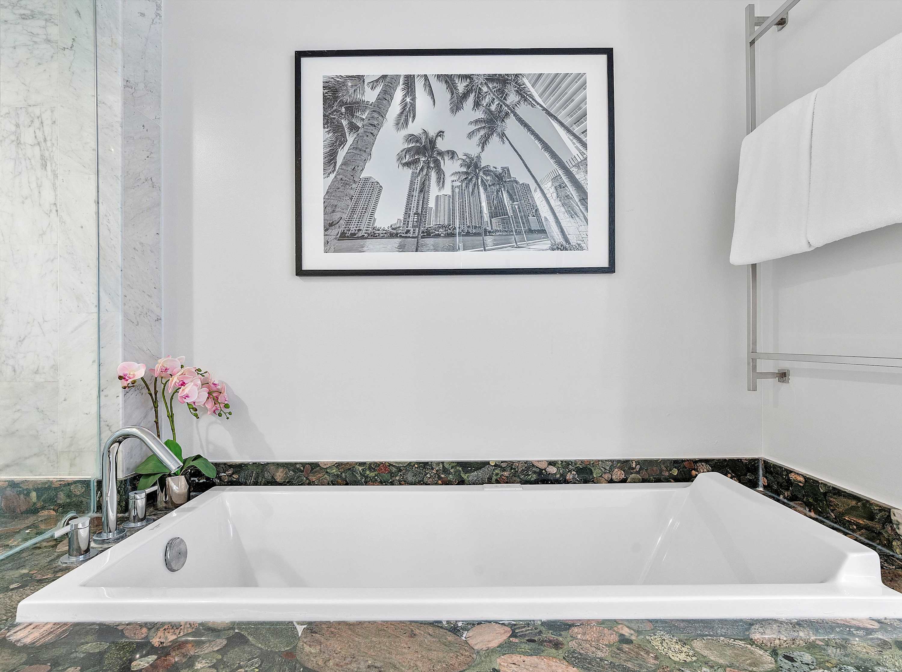 Close-up view of the deep soaking tub set into a dark marble surround, with a modern faucet and a framed black and white cityscape artwork above.