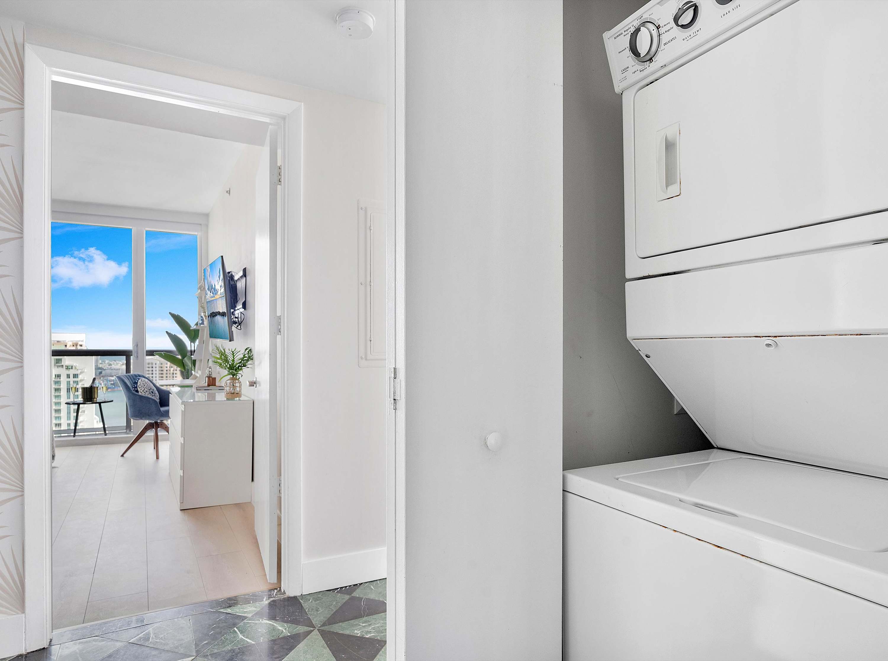 Narrow hallway featuring a stacked white washer and dryer unit, with a glimpse into another room with large windows and a city view.