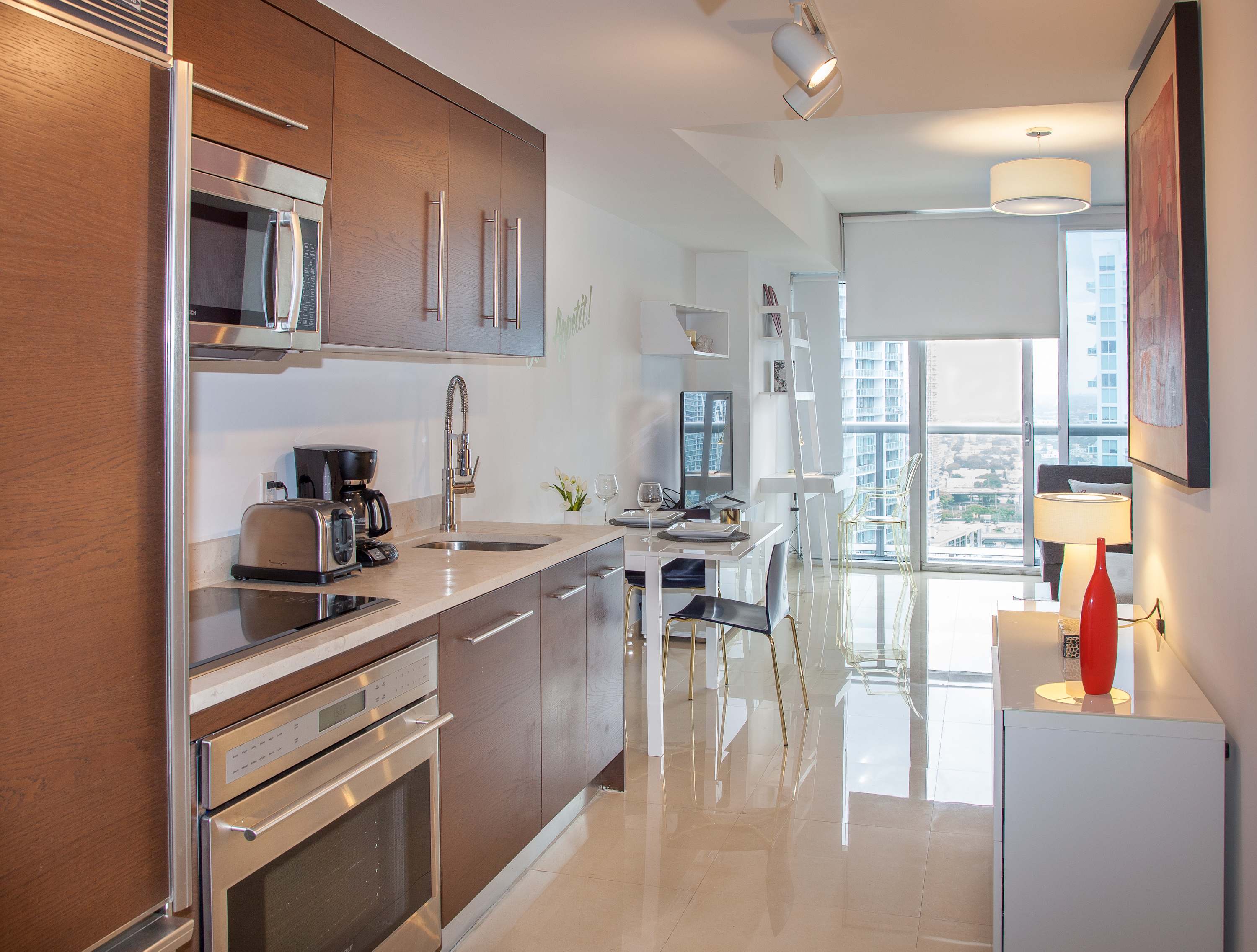 A sleek, open-concept kitchen featuring dark wood cabinetry, stainless steel appliances including a microwave and oven, and light granite countertops. A toaster and coffee maker are visible on the counter.