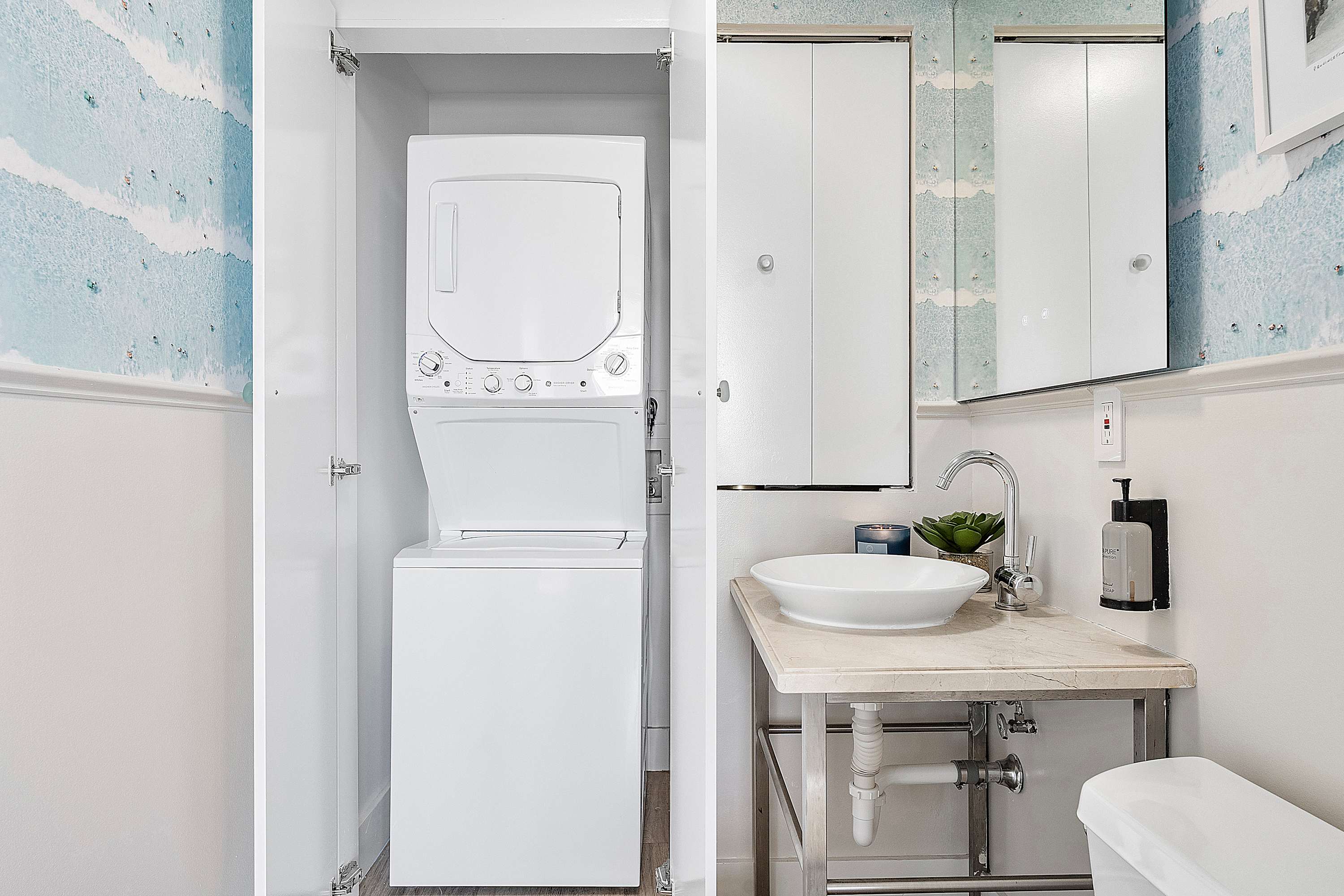 Compact bathroom featuring a vessel sink on a marble-topped vanity, a wall-mounted mirror, and a stacked washer and dryer unit neatly tucked away in a closet.