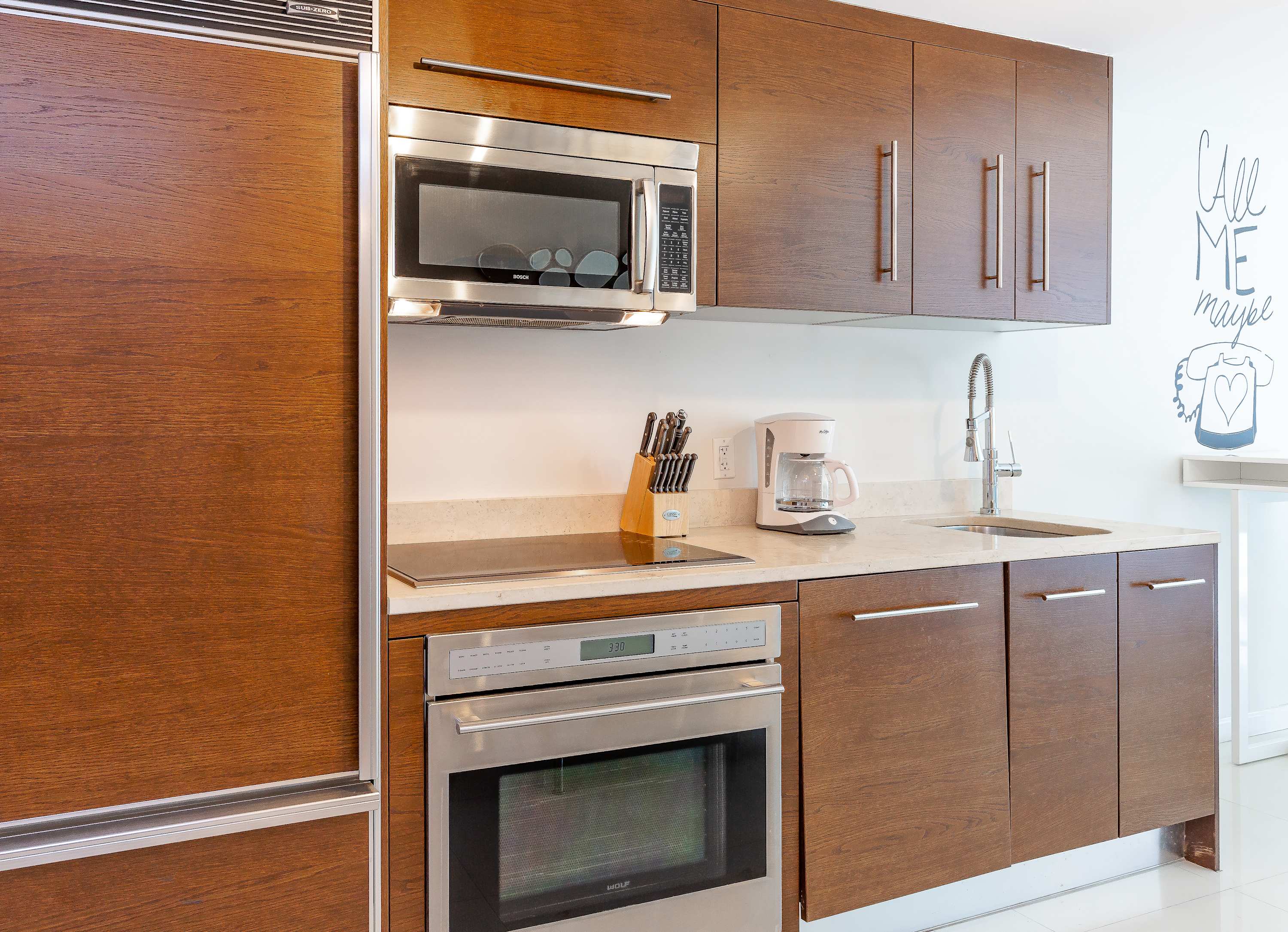 Detailed view of the modern kitchen featuring dark wood flat-panel cabinets, integrated stainless steel appliances, a built-in refrigerator, and a light stone countertop with an induction cooktop.