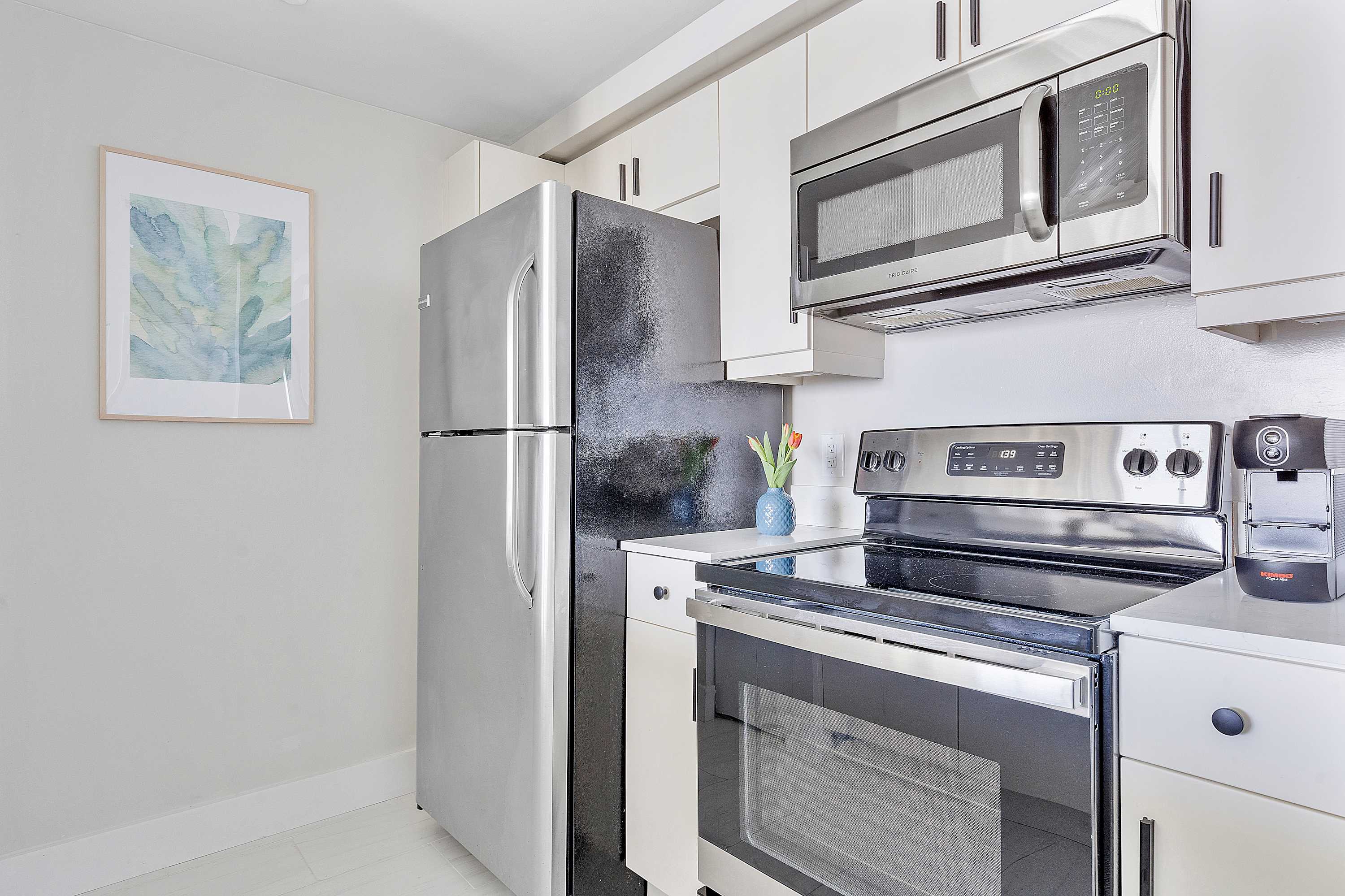Close-up of a compact kitchen area featuring stainless steel appliances including a refrigerator, microwave, and electric range, with white cabinets and countertops.