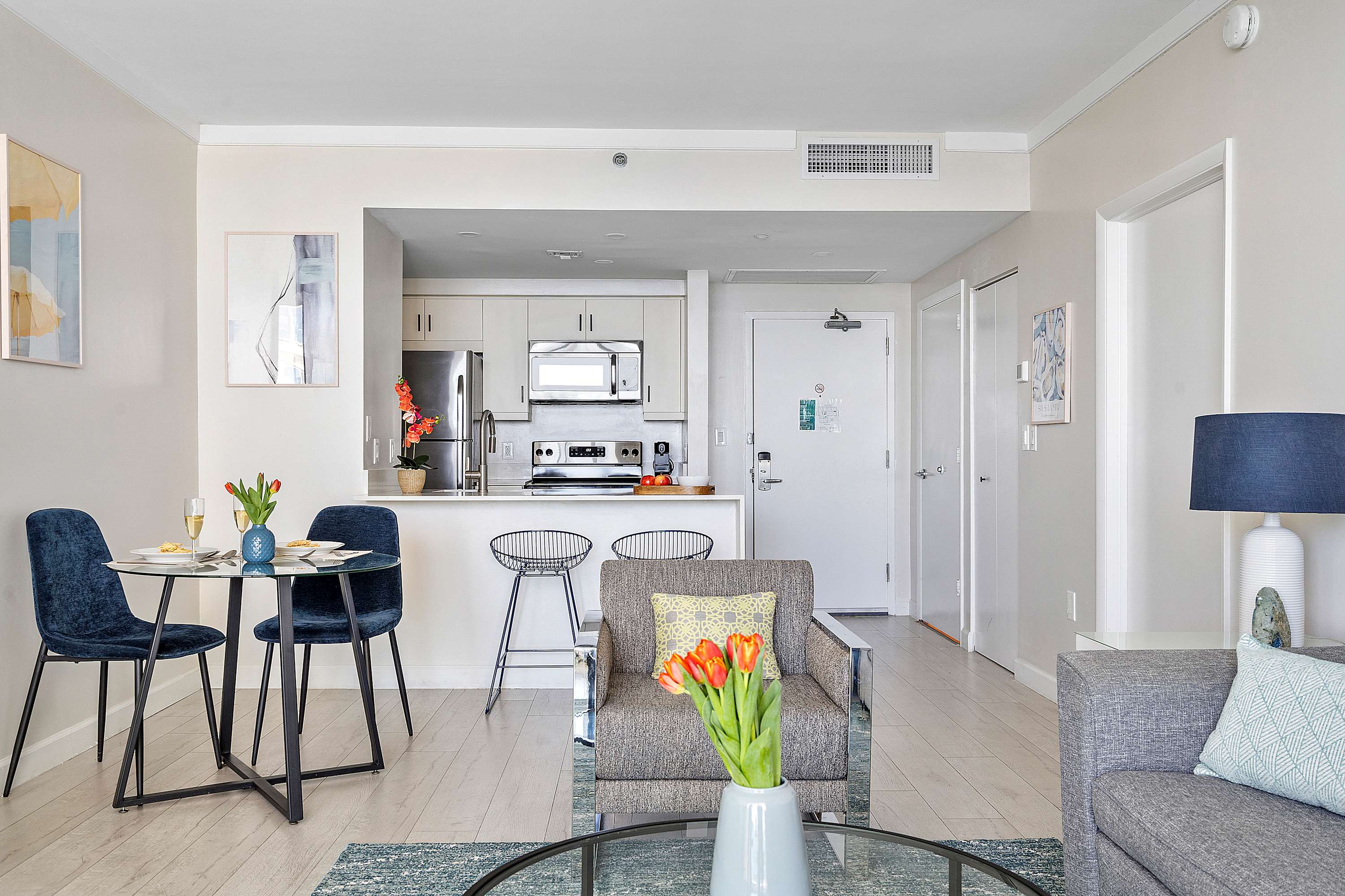 View of a modern kitchen with white shaker cabinets, stainless steel appliances, a white countertop island with bar stools, and a small dining table in the foreground.