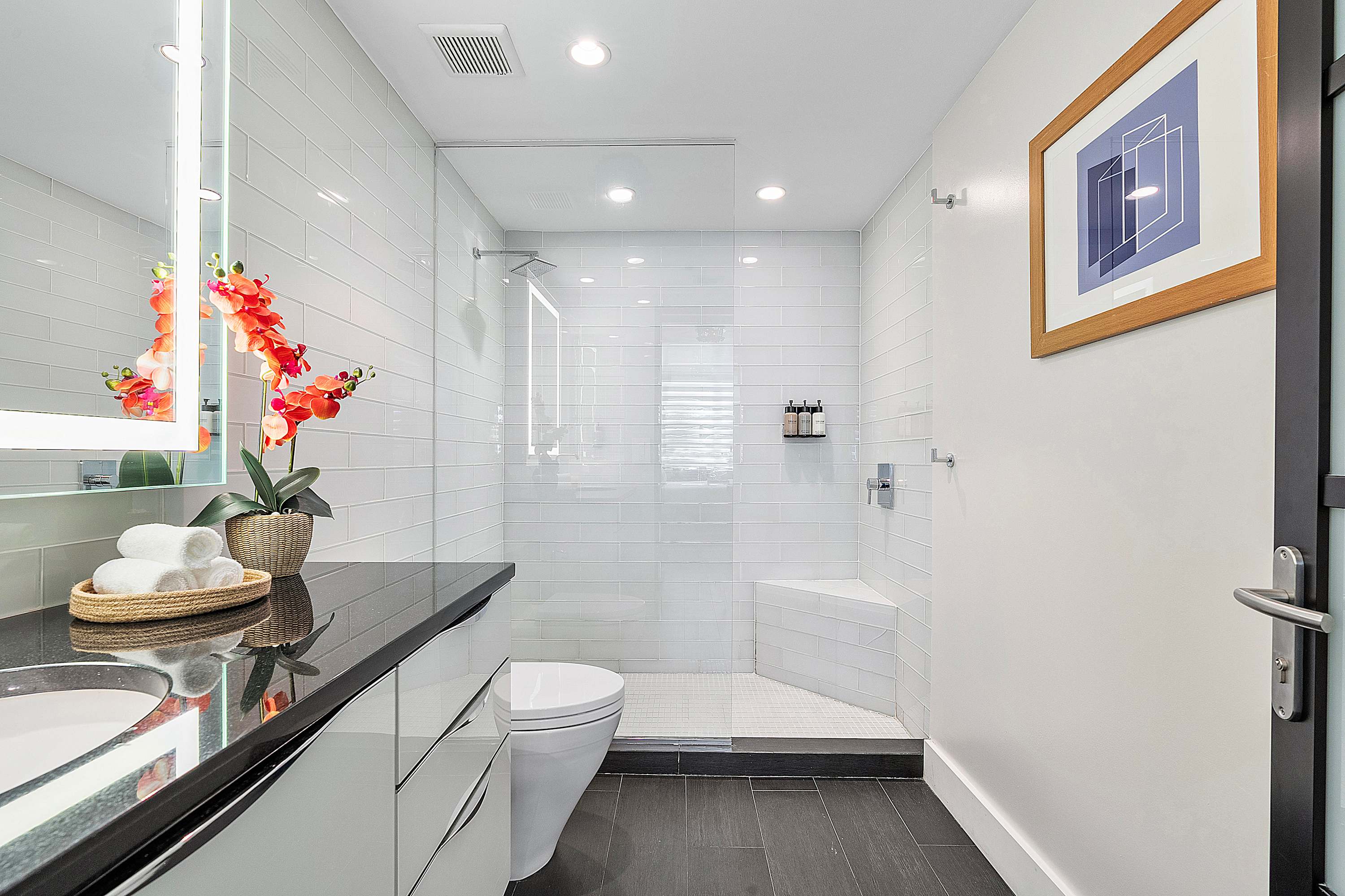 Contemporary bathroom featuring a walk-in shower with a glass enclosure, white subway tiles, and a built-in bench. A toilet is visible next to the shower, and dark floor tiles complete the look.