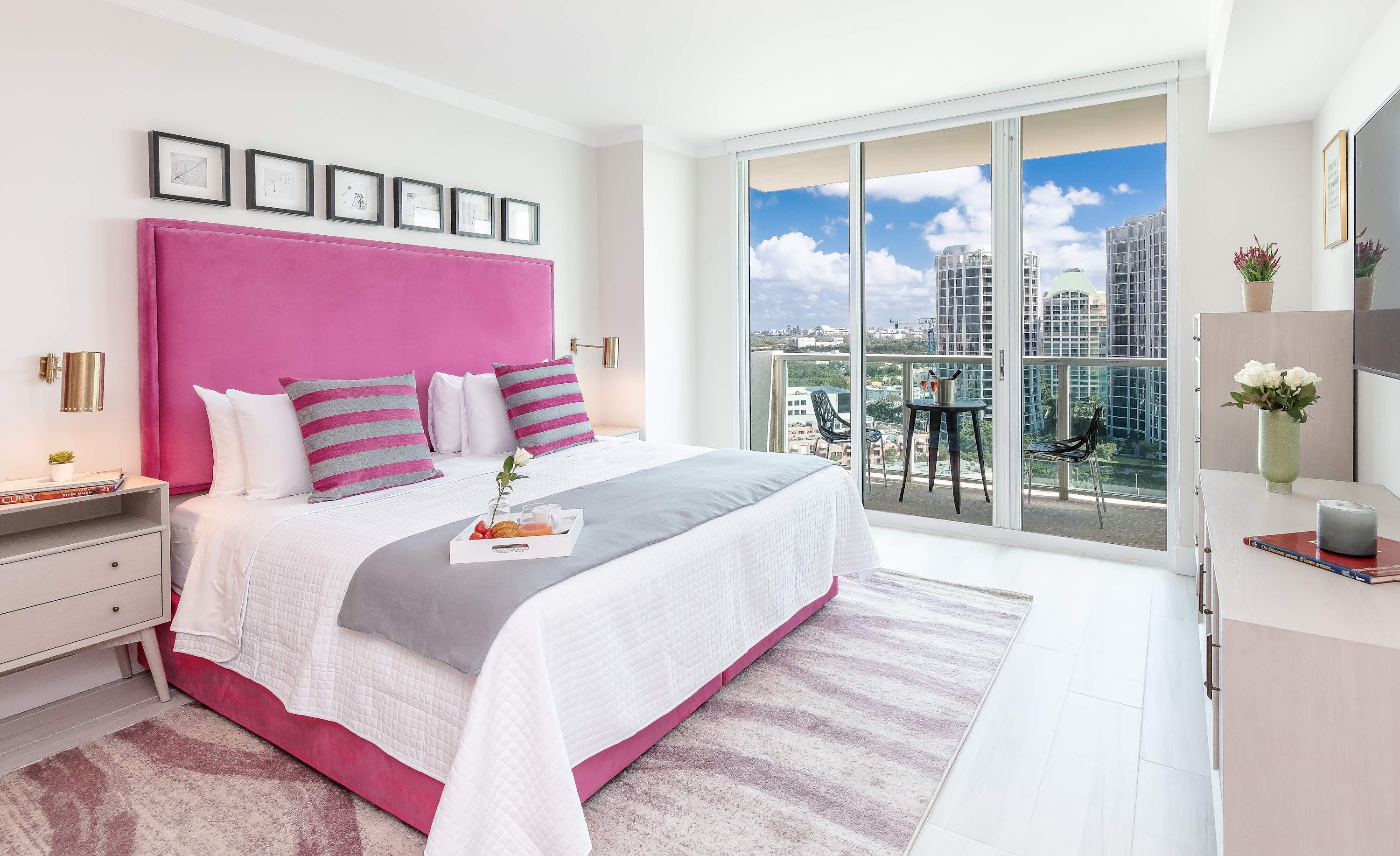 The king-sized bed with a hot pink headboard faces a dresser and a large sliding glass door leading to a private balcony with city views.