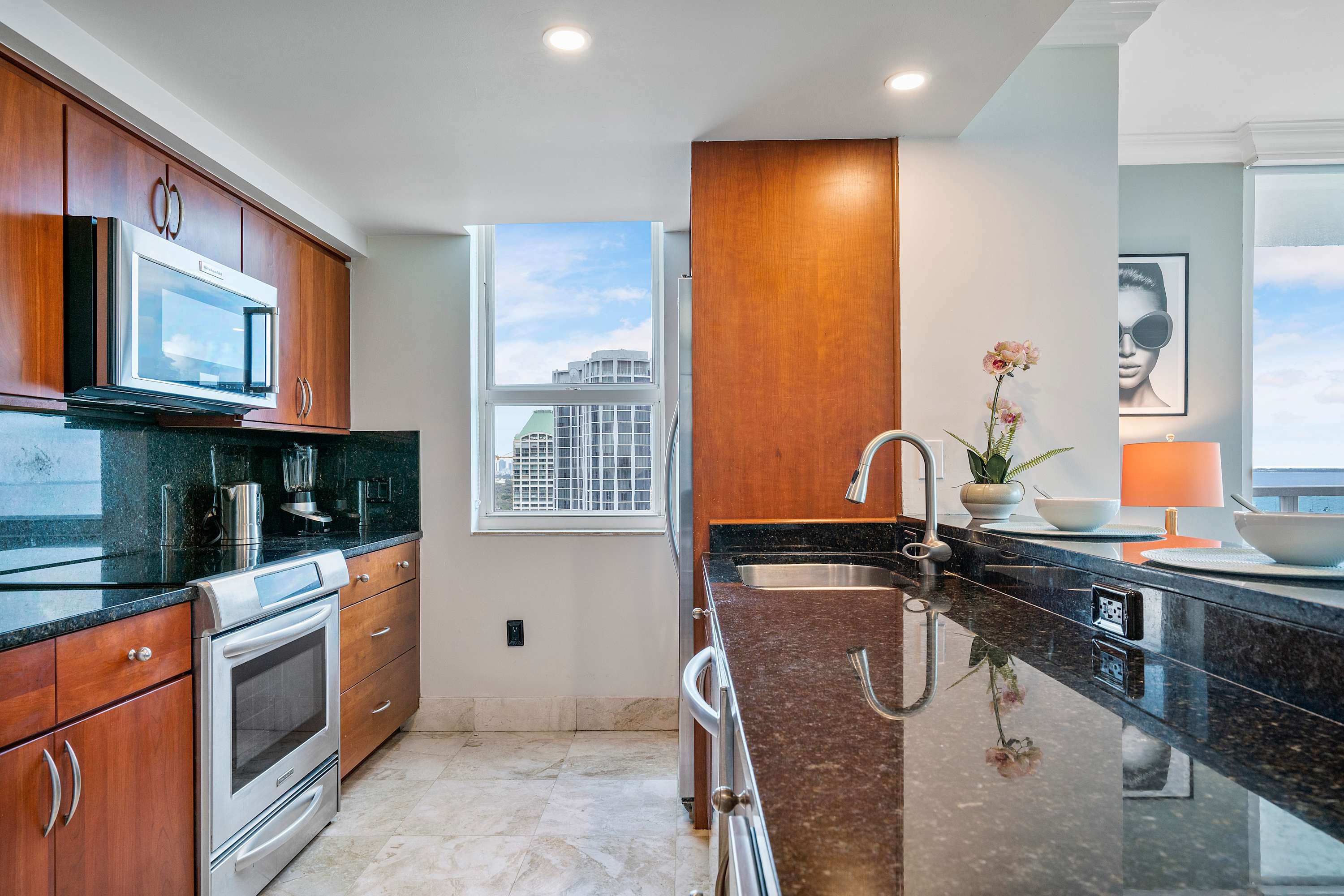 Well-equipped kitchen featuring dark wood cabinets, black granite countertops, stainless steel appliances including an oven and microwave, and a window providing a city view.