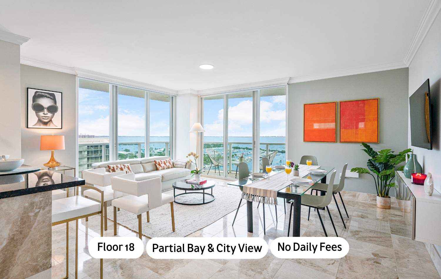 Bright, open-concept living and dining area with floor-to-ceiling windows offering partial bay and city views, featuring a light-colored sofa, a glass dining table, and modern decor on marble floors.