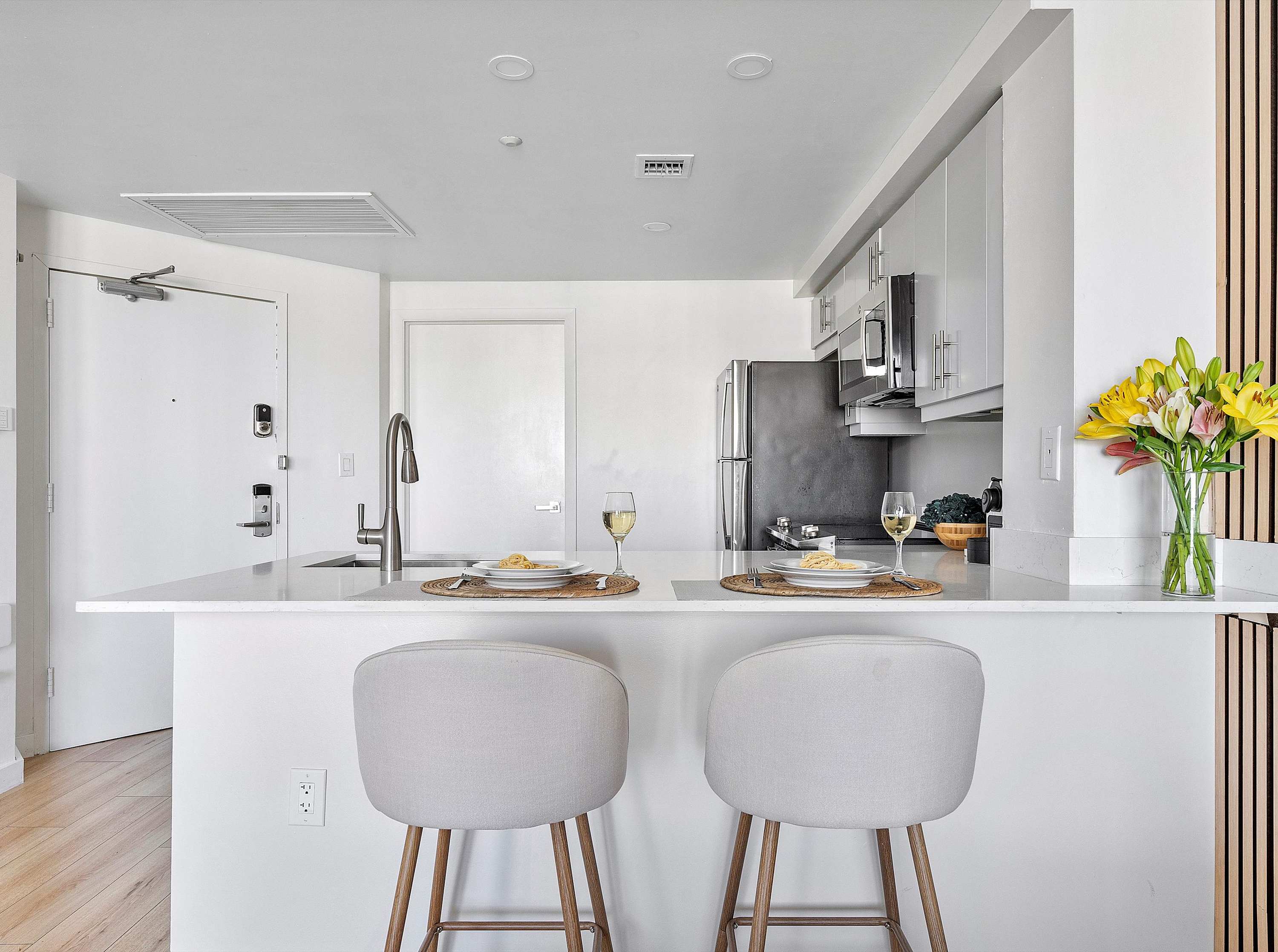 A detailed view of the kitchen island, featuring a white quartz countertop, a sink with a modern faucet, and two light-colored bar stools with place settings, ready for dining.