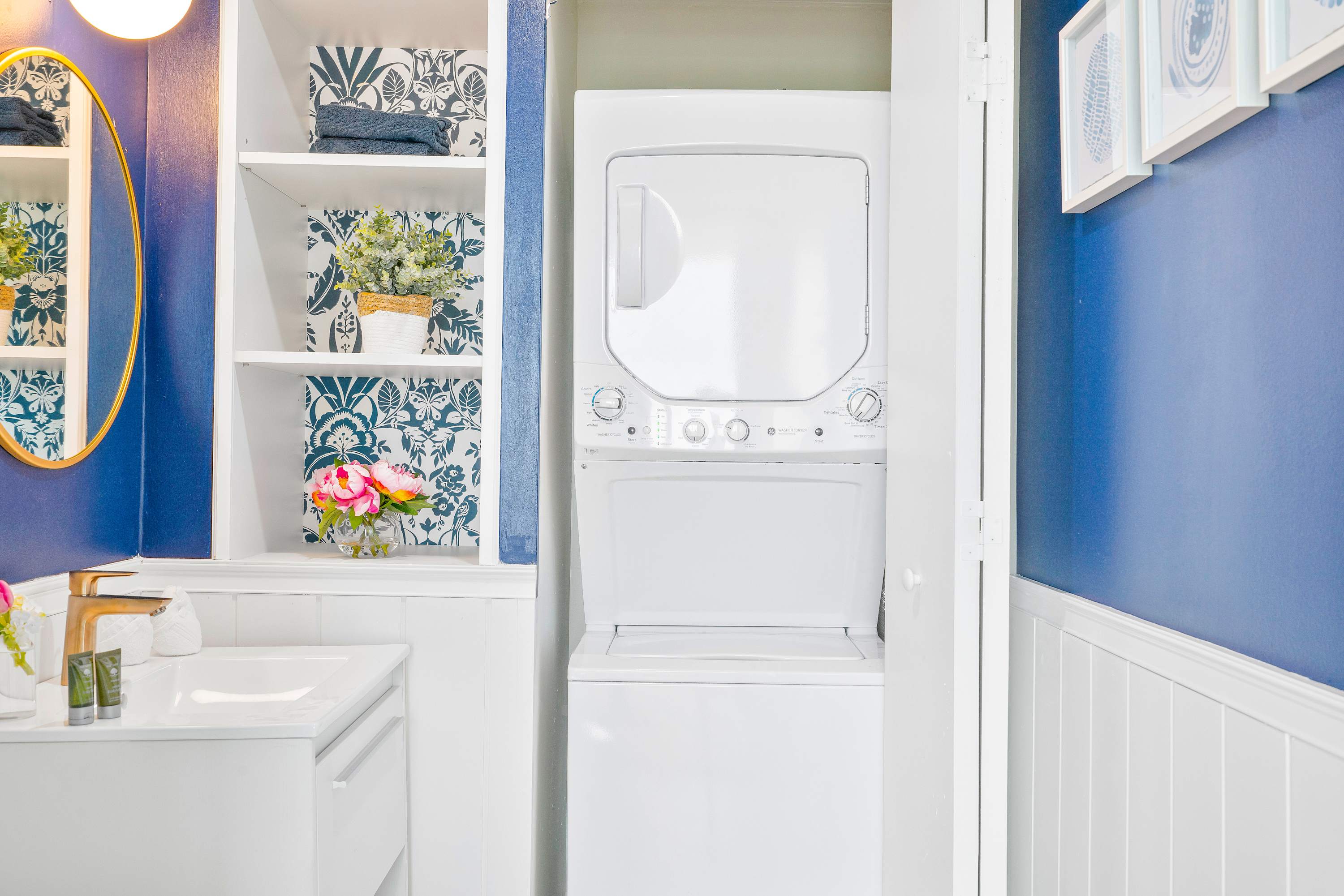 Compact laundry area featuring a white stacked washer and dryer unit, set within a closet with a blue and white patterned wall and white shelving.