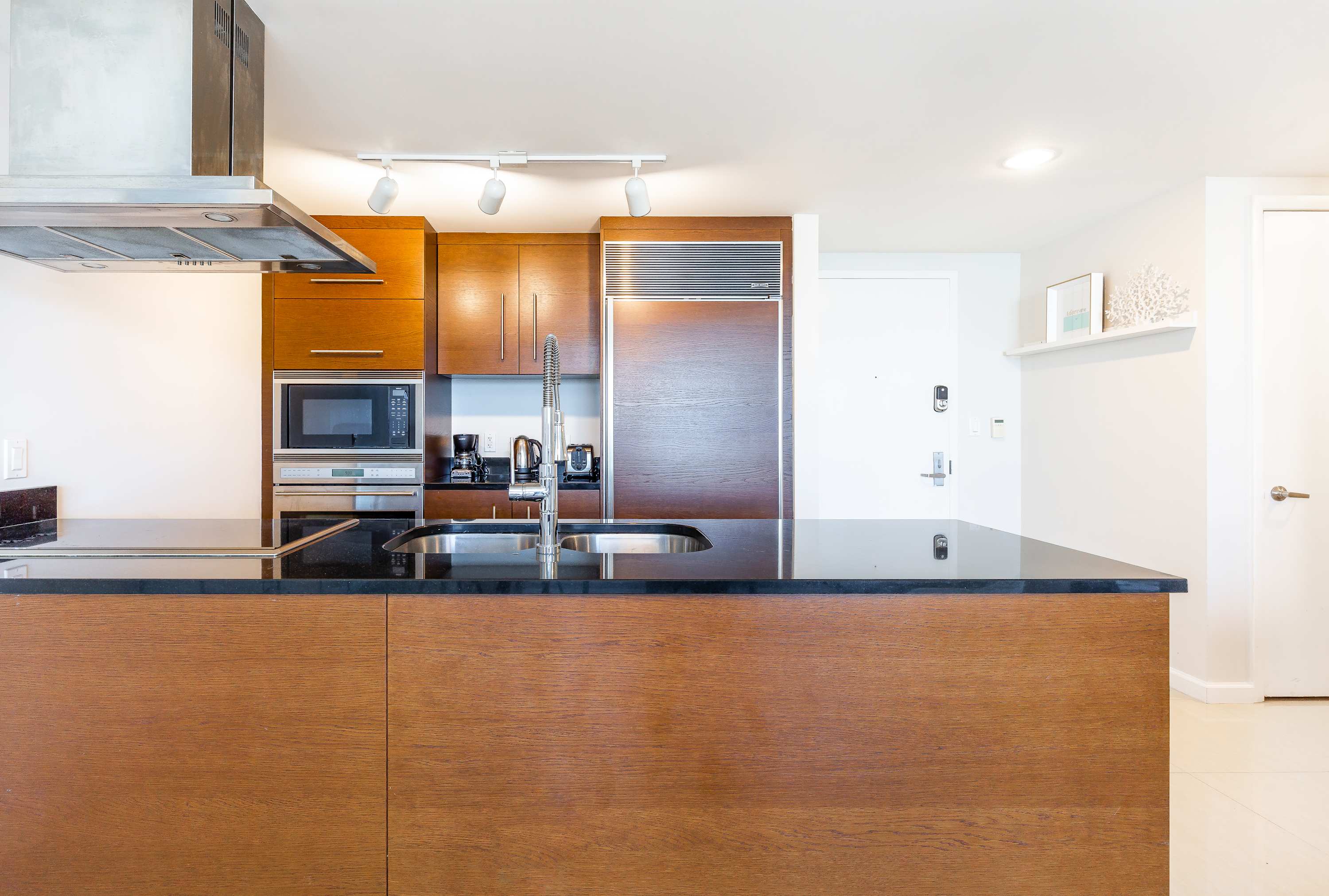 Contemporary kitchen featuring dark wood cabinetry, a black granite island with a sink, and stainless steel appliances including a microwave and oven.