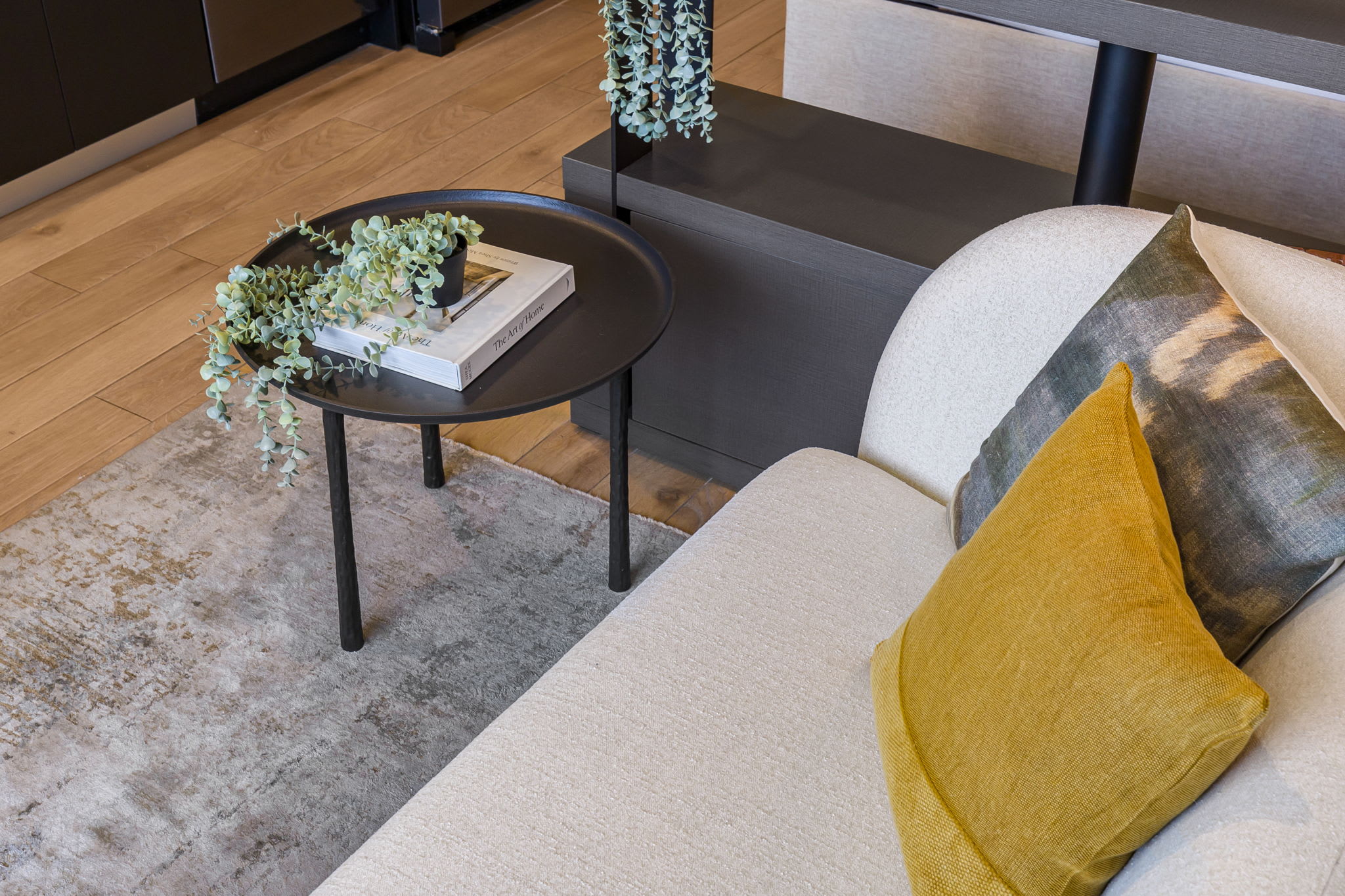 Overhead perspective of the living room, showcasing a textured area rug, a light-colored sofa with a mustard yellow pillow, and a dark round side table adorned with books and a small plant.