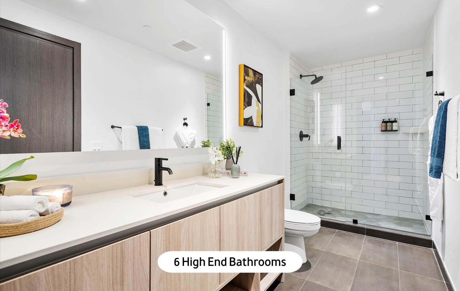 A modern and bright bathroom featuring a long vanity with a single sink, a large mirror with integrated lighting, and a spacious walk-in shower with white subway tiles and a glass enclosure.