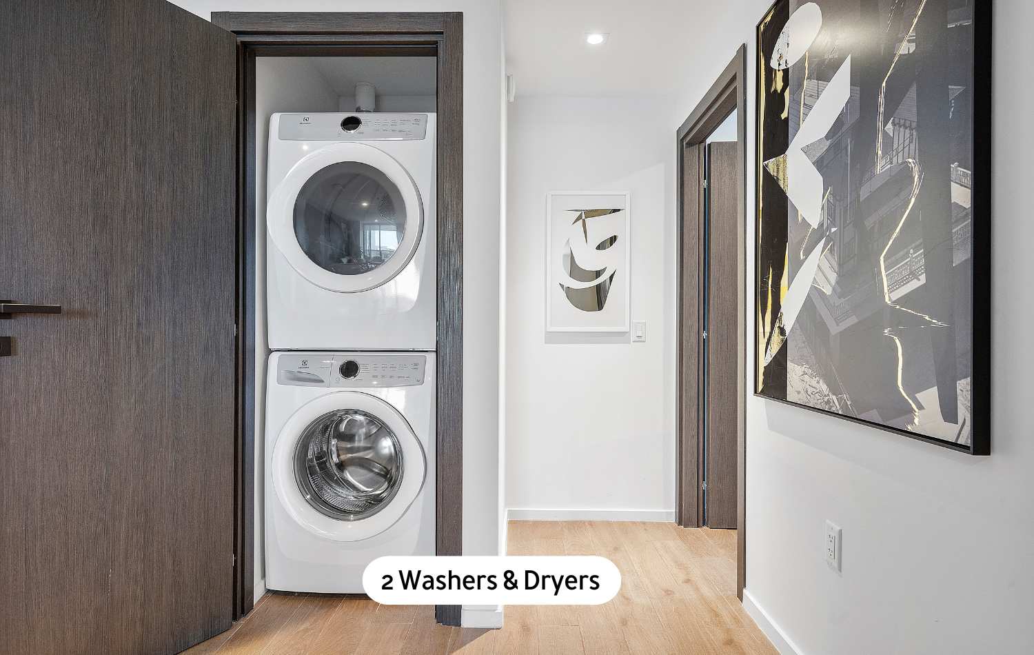 A compact laundry area neatly tucked into a closet, featuring a stacked white washer and dryer unit, set against light walls and light wood flooring in a hallway.