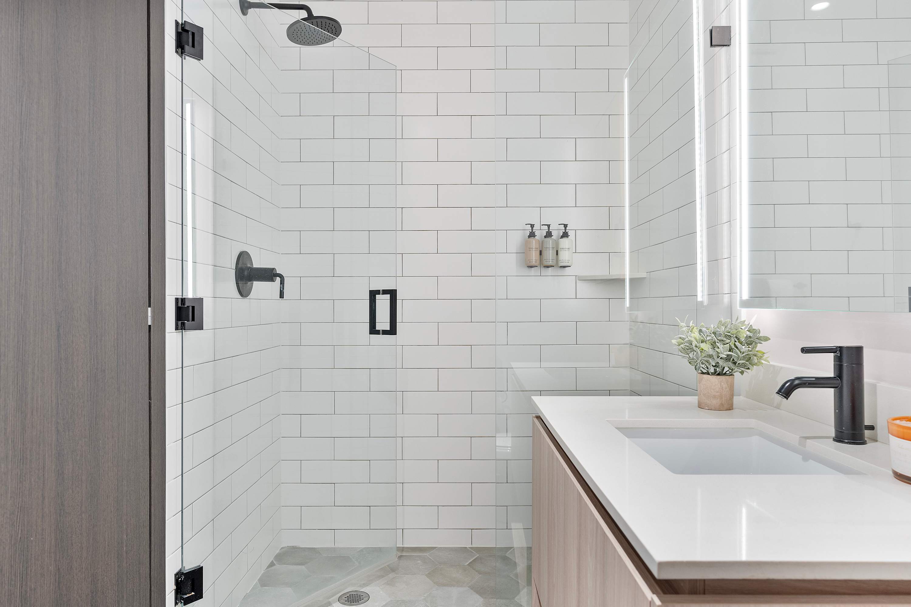 Contemporary bathroom-1 featuring a spacious walk-in shower with white subway tiles, a glass enclosure, a black rain shower head, and hexagon-patterned floor tiles.