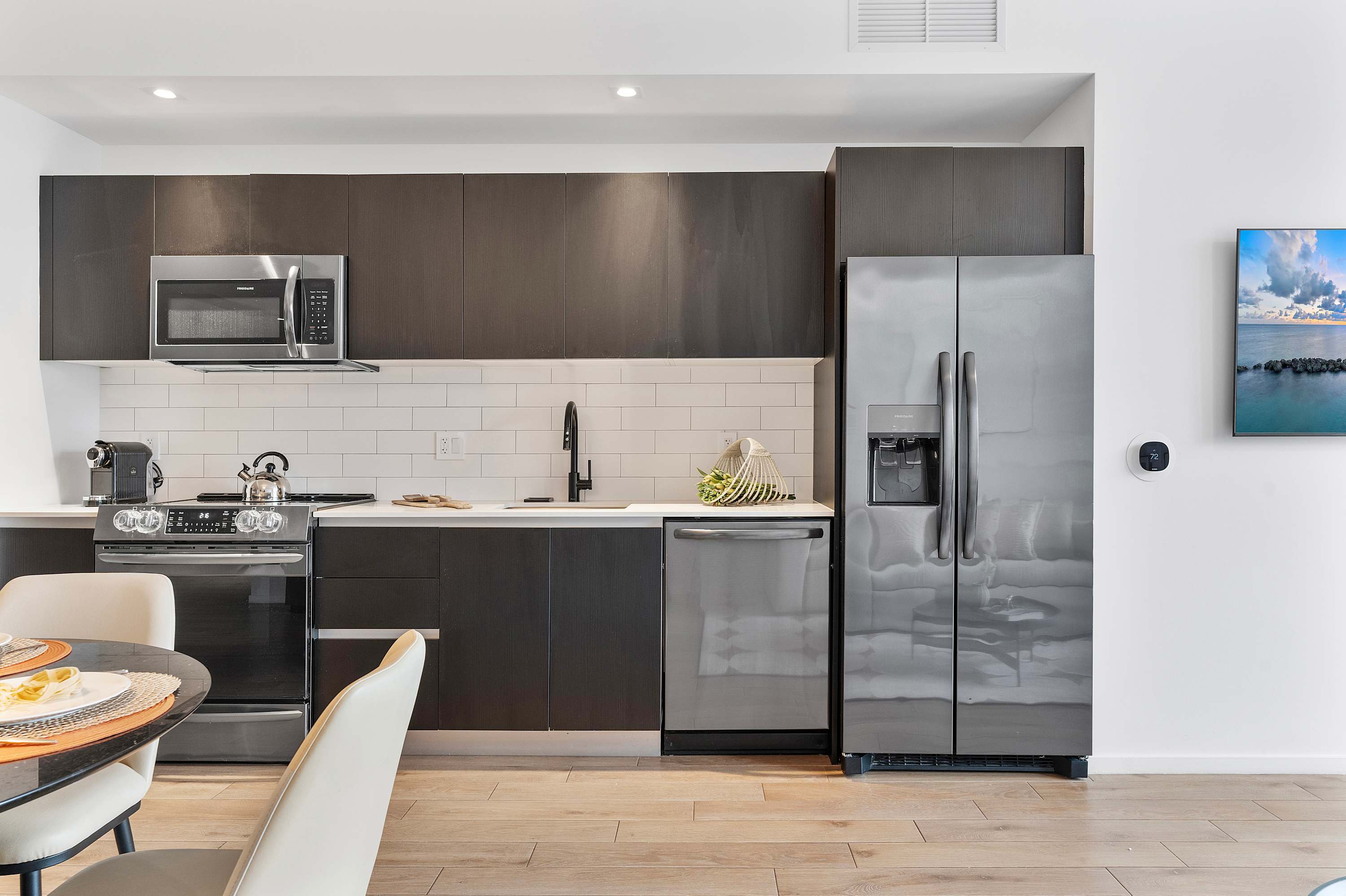 Modern kitchen with dark flat-panel cabinetry, white subway tile backsplash, stainless steel appliances including a refrigerator, oven, microwave, and dishwasher, and a black sink with a gooseneck faucet.