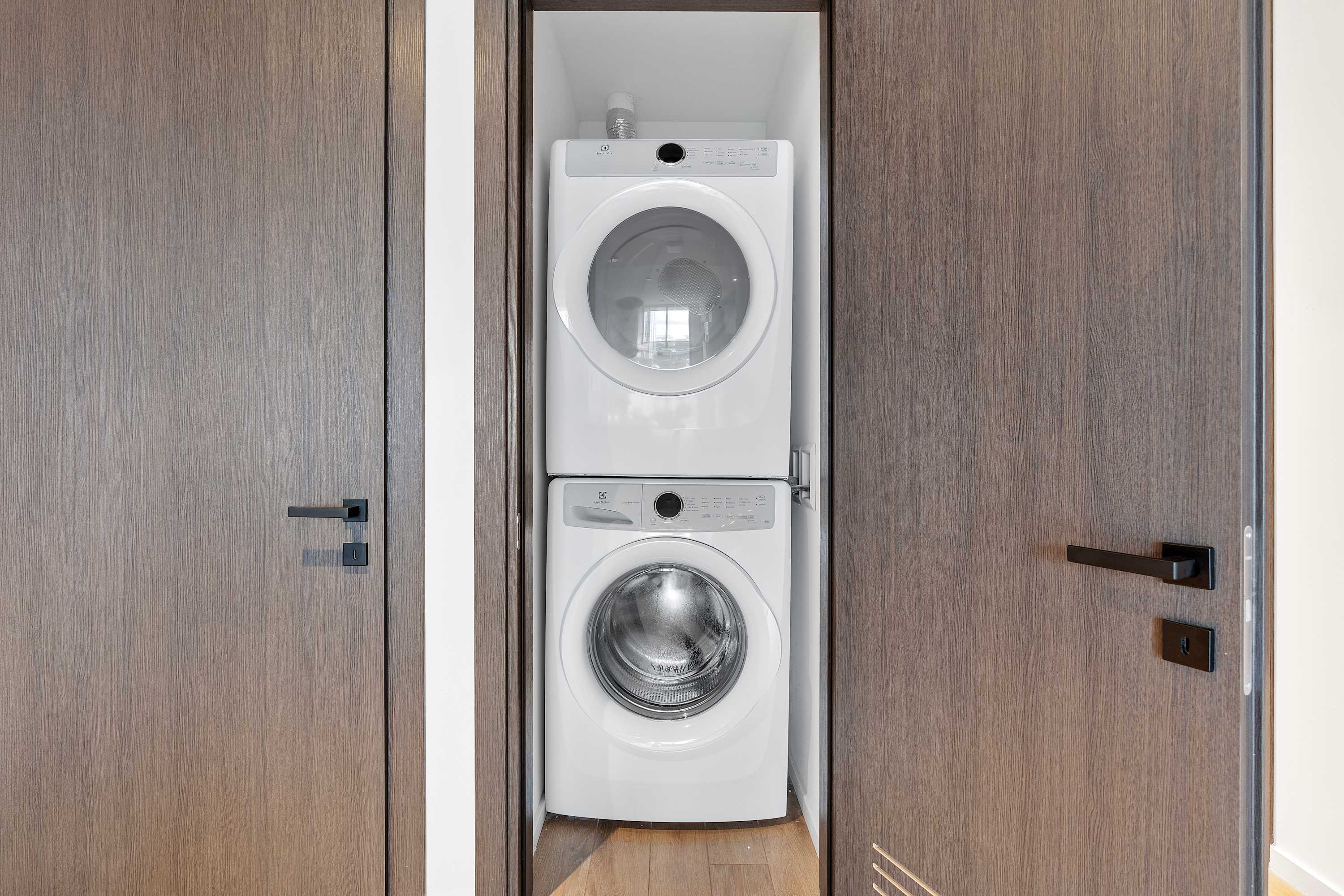 A white stacked washer and dryer unit is neatly tucked into a closet with dark wood doors, providing a compact and functional laundry space.