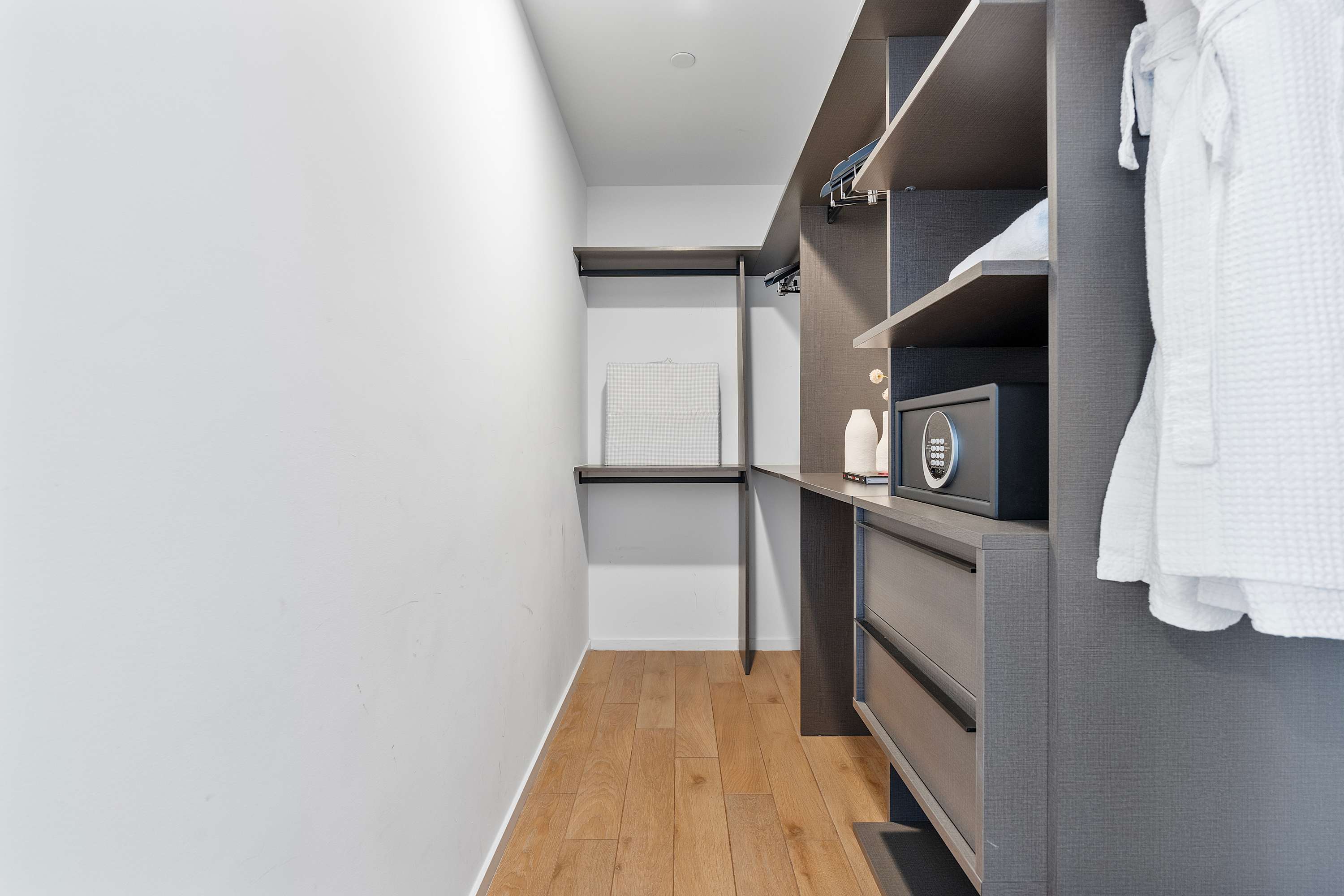 Organized walk-in closet with dark wood shelving, drawers, and hanging rods, including a small safe, offering ample storage space.