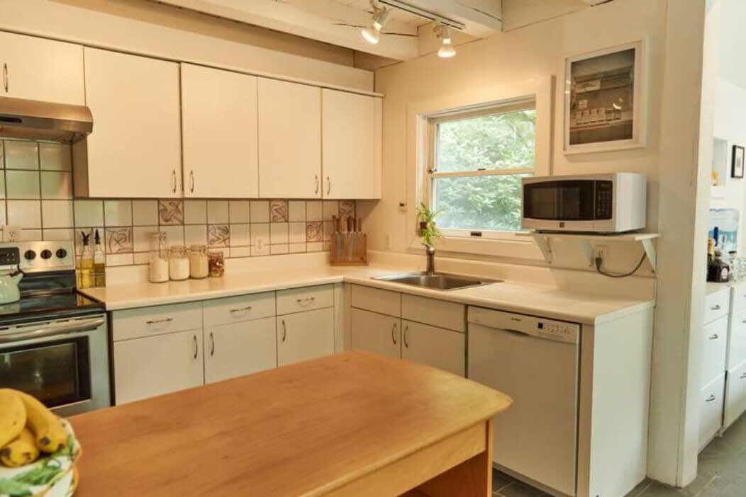 Cozy kitchen with white cabinetry, light countertops, and a white tiled backsplash with decorative accents. Appliances include a stainless steel range, microwave, and dishwasher, with a wooden island in the foreground.