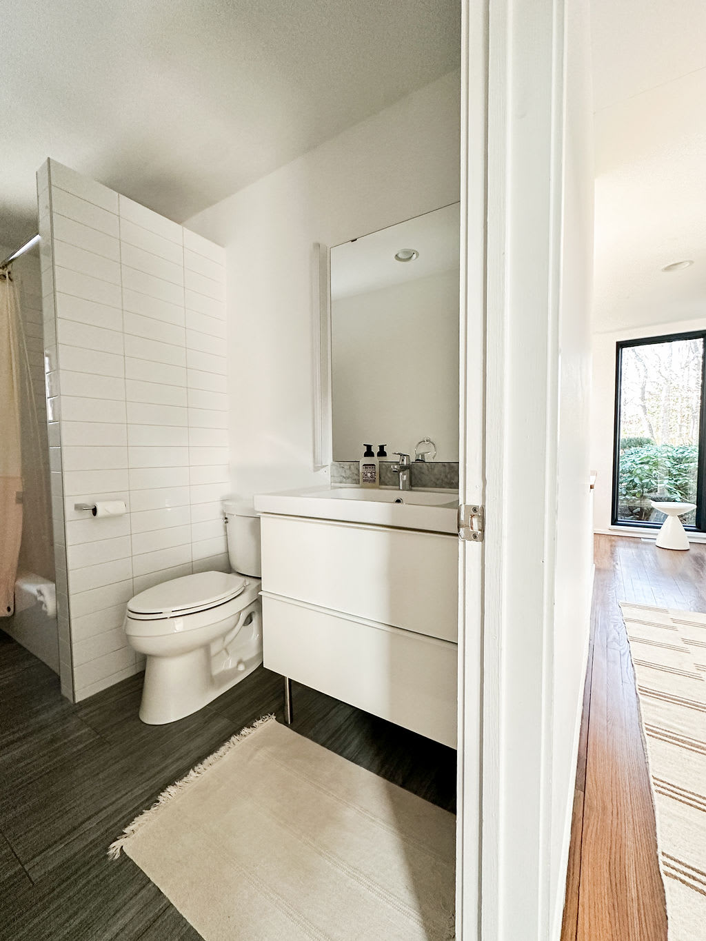 Bright bathroom featuring a white floating vanity, toilet, and a shower/tub combo with white subway tile walls. Dark gray floor tiles contrast with the clean white fixtures.