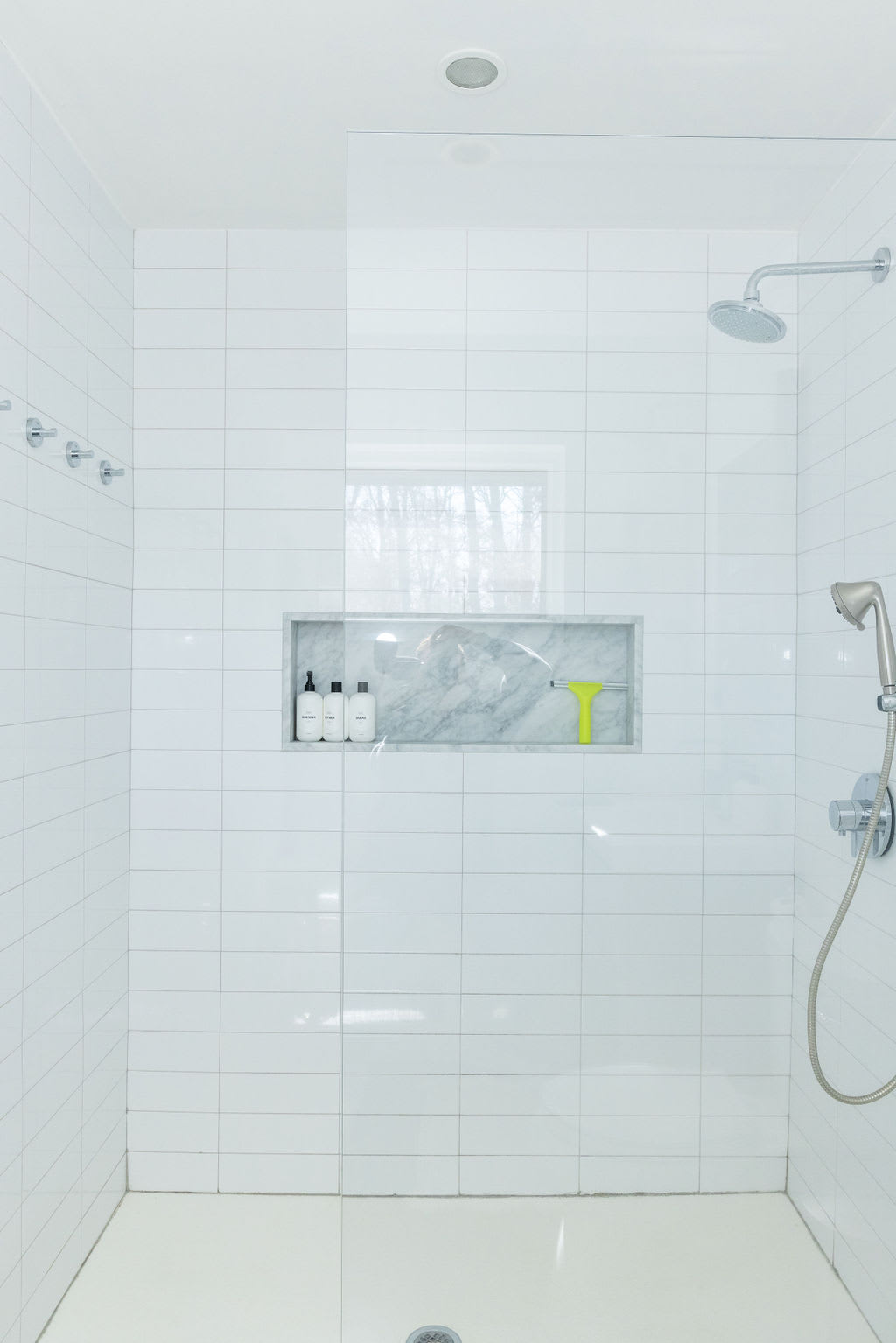 Close-up view of a spacious walk-in shower with white subway tiles, a built-in marble niche for toiletries, a rain shower head, and a handheld shower sprayer.