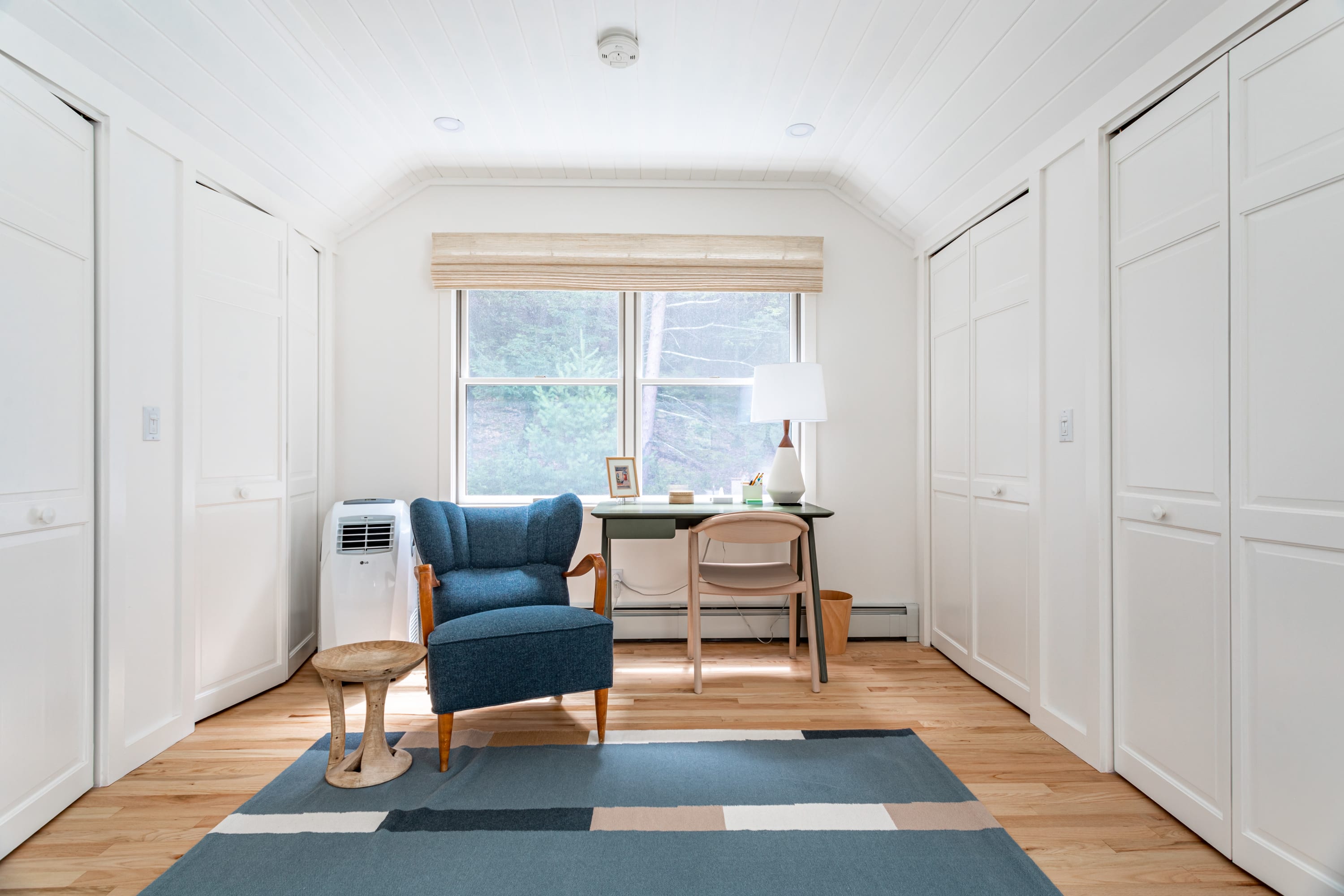 The dedicated workspace within bedroom-3, featuring a blue armchair, a modern desk with a chair, and a large window overlooking trees. White bi-fold closet doors line the walls.