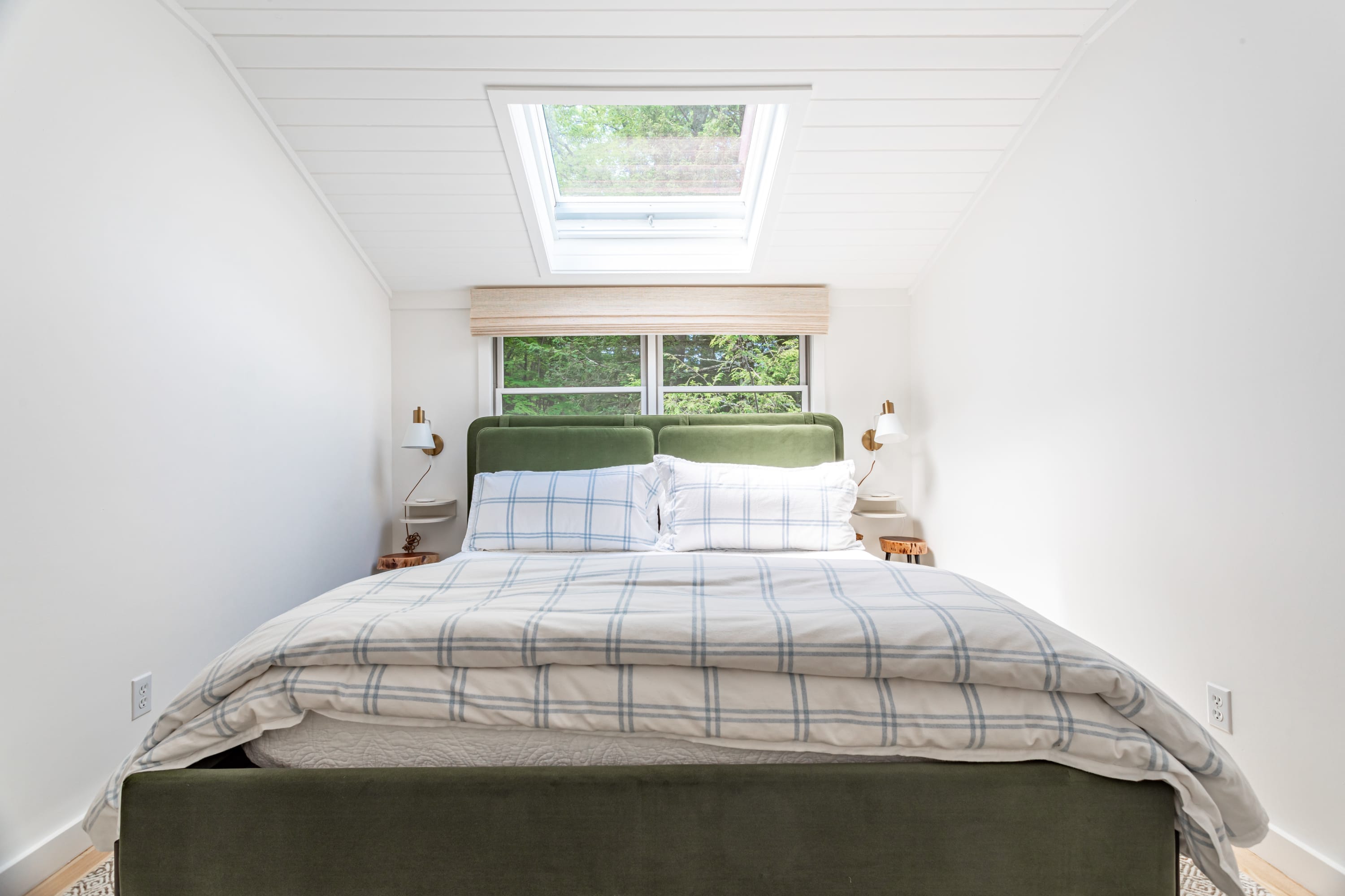 The sleeping area of bedroom-3, featuring a green upholstered bed with plaid bedding, white walls, and a prominent skylight above. Bedside tables with lamps flank the bed.