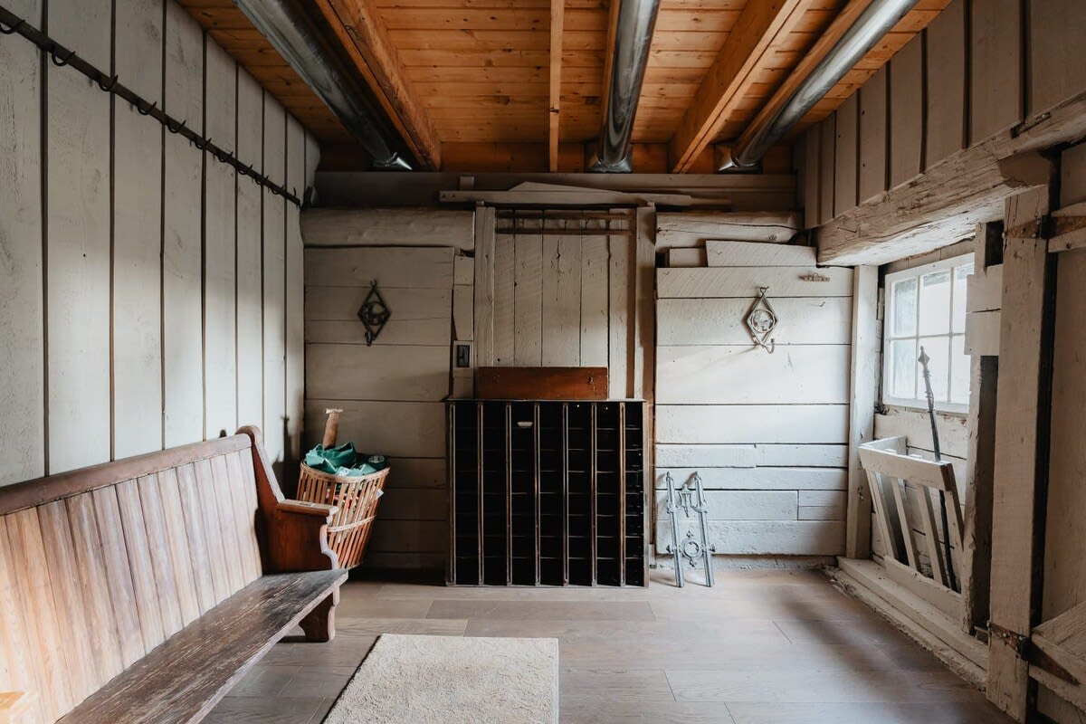 A rustic entryway or mudroom with white-washed wooden plank walls, exposed ceiling beams, a long wooden bench, and a multi-compartment storage unit.