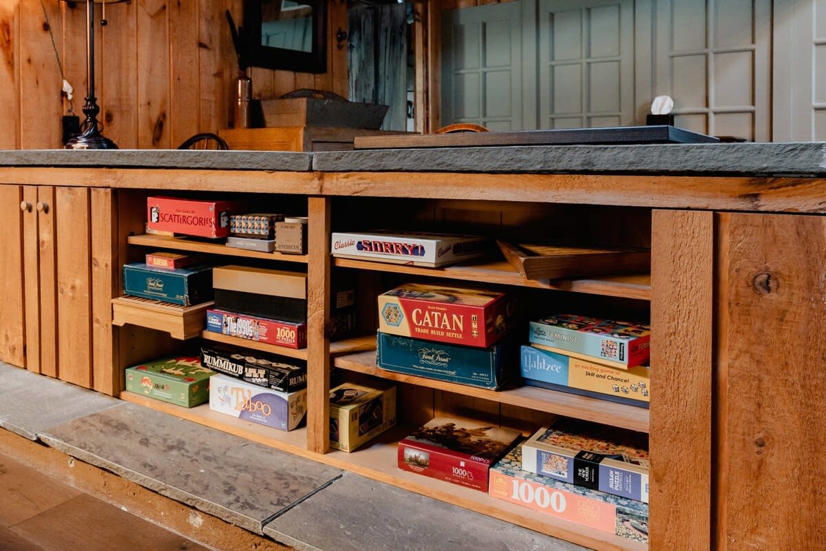 Built-in shelving unit filled with a variety of board games and puzzles, indicating a dedicated entertainment or game area. The unit is made of natural wood with a stone countertop.